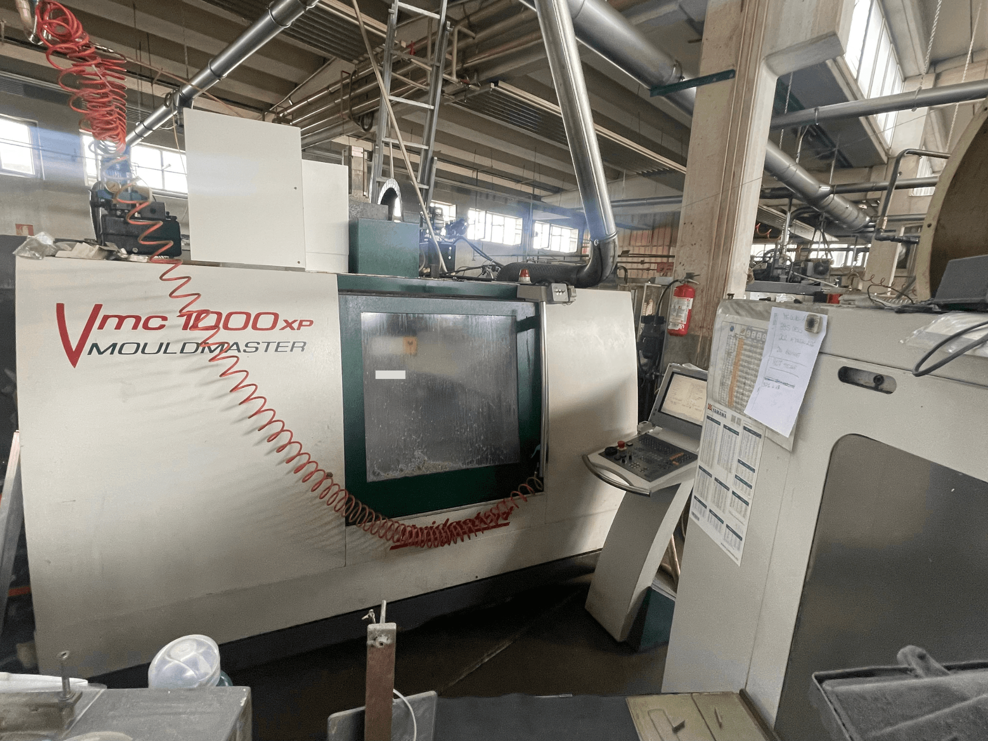 Vertikalusis apdirbimo centras „Bridgeport VMC 1000“, vaizdas iš priekio, kuriame matomas valdymo pultas ir staklių detalės pramoninėje aplinkoje.