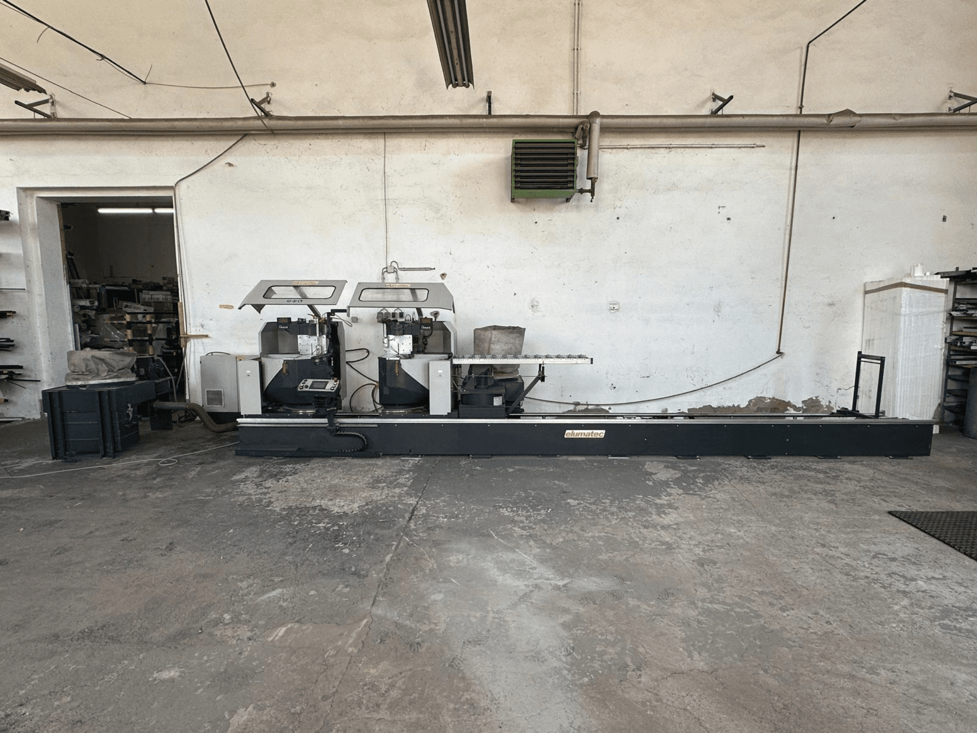 Elumatec DG 244 diskinis metalo pjūklas dirbtuvėse, šoninis vaizdas, kuriame matyti du pjūklai ir valdymo įtaisai ant tvirto pagrindo.