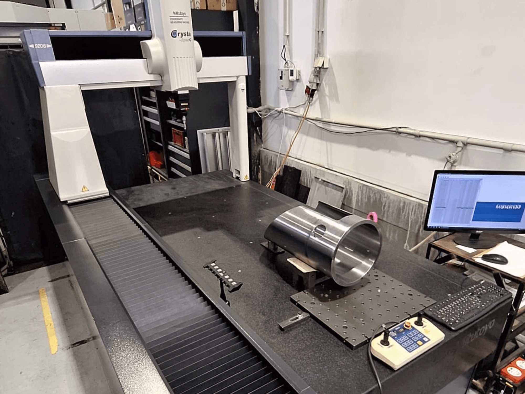 Mitutoyo Crysta-Apex C9206 KMM iš priekio, matuojant cilindrinę metalinę detalę ant juodo granito paviršiaus plokštės.