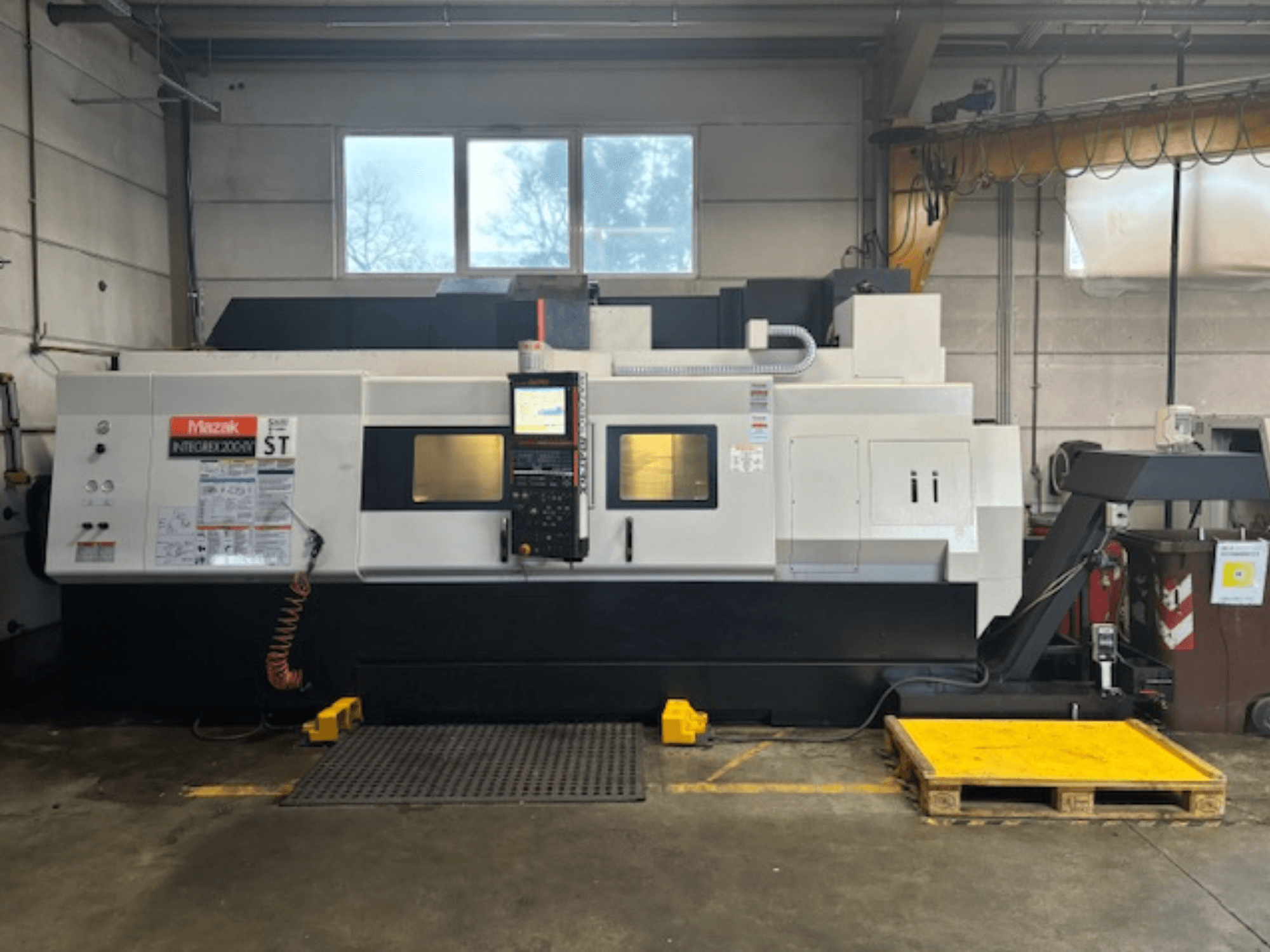 Mazak Integrex 200 SY ST, šoninis vaizdas, kuriame matomas valdymo skydelis, veikimo ekranai ir aušinimo skysčio linijos dirbtuvėse.