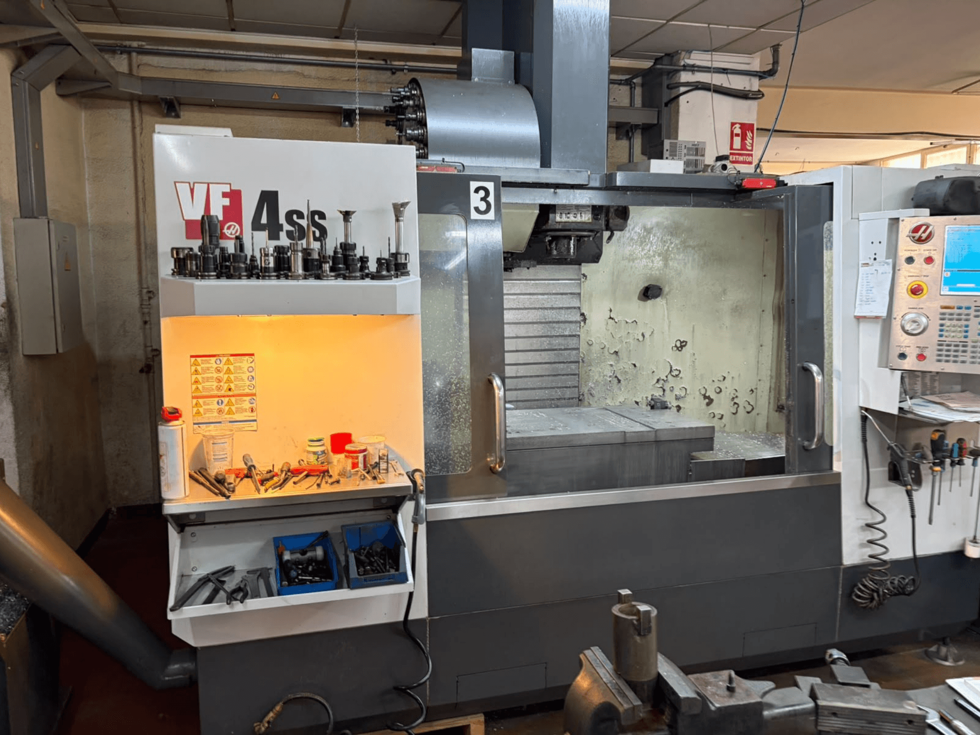 Vertikalusis apdirbimo centras „HAAS VP 4SS“, vaizdas iš priekio: matyti įrankių saugykla, valdymo pultas ir apdirbimo detalėmis papuošta matoma darbo zona.
