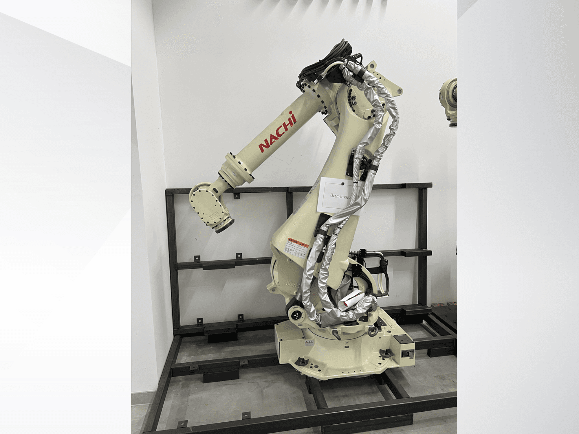 NACHI SRA166-01 roboto rankos vaizdas iš šono, su lanksčiomis jungtimis, pritvirtintais kabeliais ir apsauginiu rėmu.