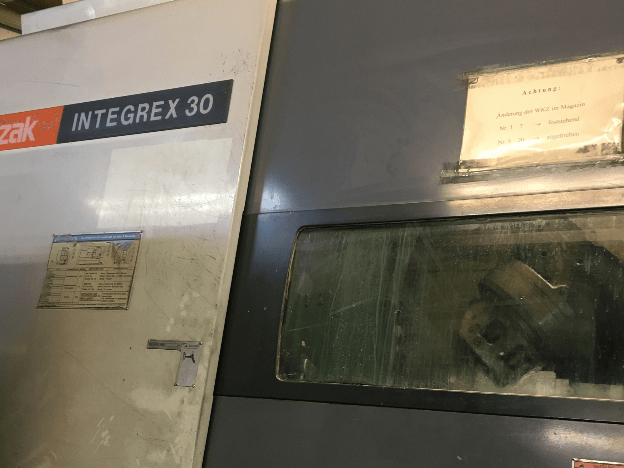 „Mazak Integrex 30 Y Universal 1000“ tekinimo ir frezavimo centro vaizdas iš priekio, kuriame matomi valdymo elementai ir pro langelį matomi įrankiai.