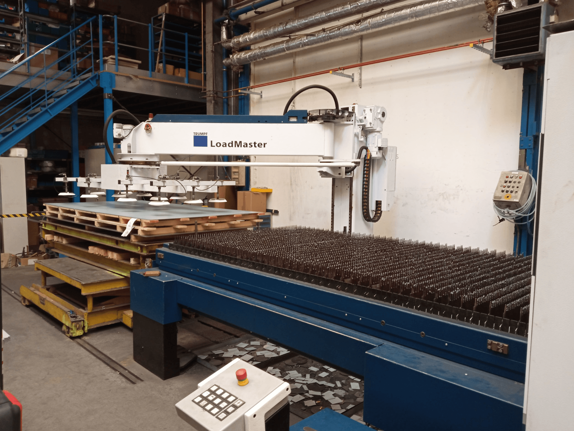 „TRUMPF TruLaser 3030“ CO₂ lazerinio pjovimo staklės, vaizduojamos iš šono, su „LoadMaster“ įrenginiu ir medžiagų padėklais.