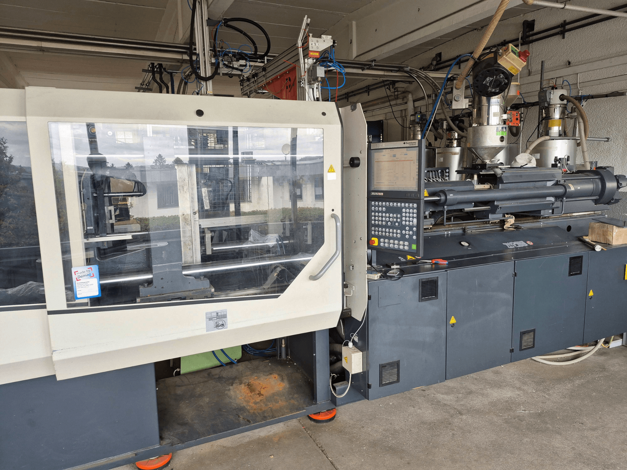 Hidraulinė liejimo mašina „SUMITOMO SHI DEMAG Systec 210/580-1450“, vaizdas iš priekio su valdymo pultu ir matomais komponentais.