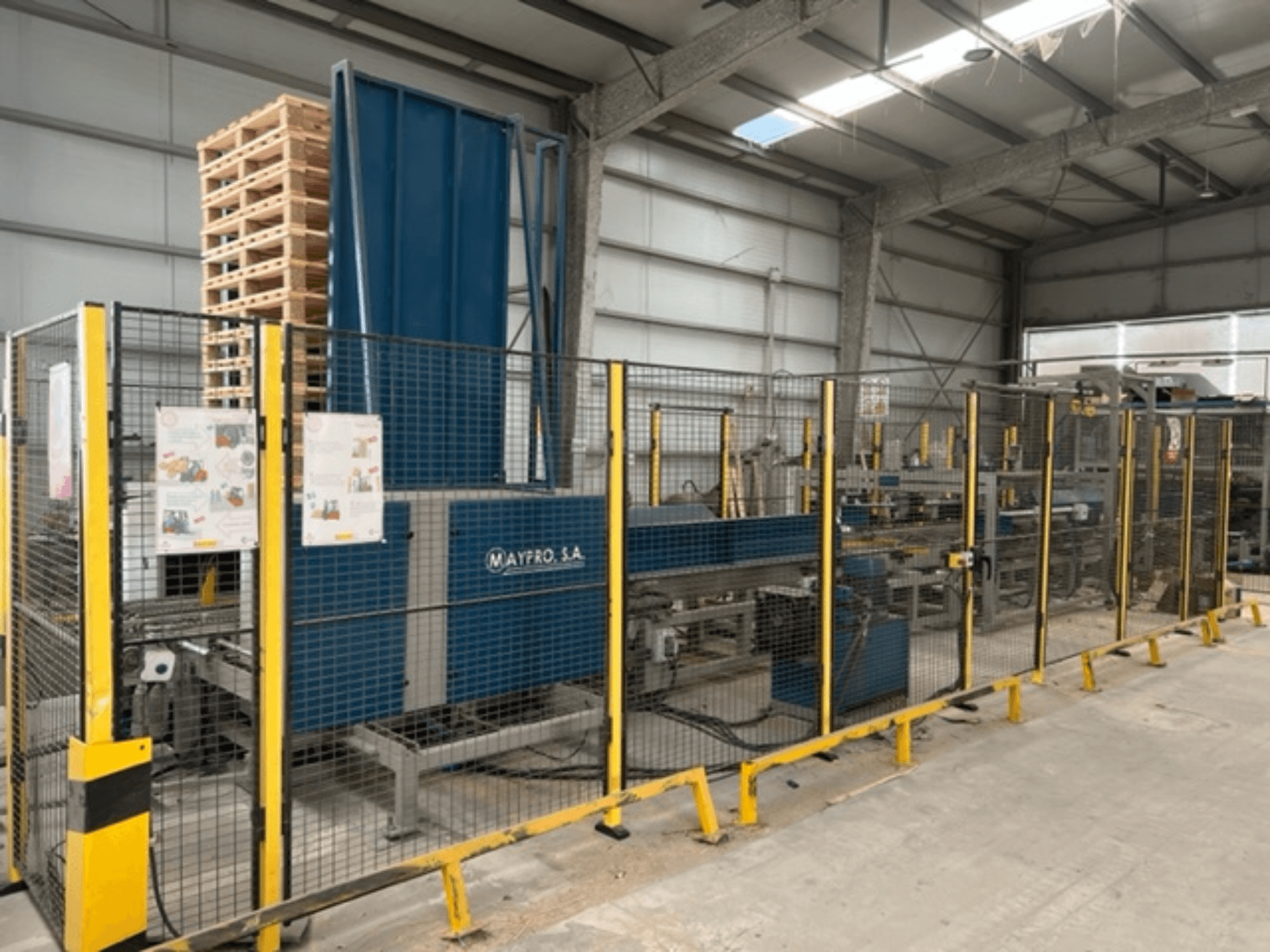 "Maypro S.A." pramoninė padėklų pakavimo mašina sandėlyje, su apsauginiu tinkleliu ir valdymo įtaisais, vaizdas iš šono.