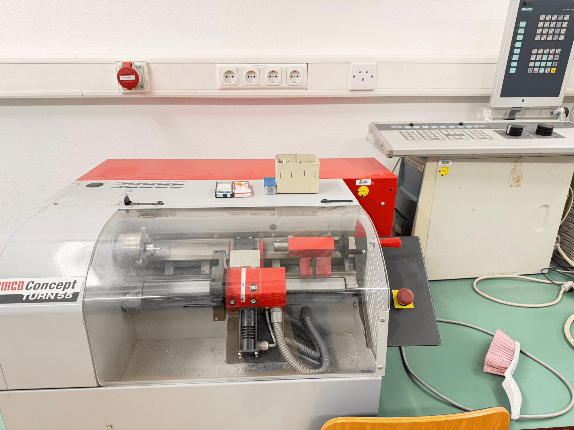 EMCO Concept Turn 55 horizontaliojo tekinimo staklės su raudona ir pilka išore, priekinis vaizdas, kuriame matomi valdikliai ir darbo zona.