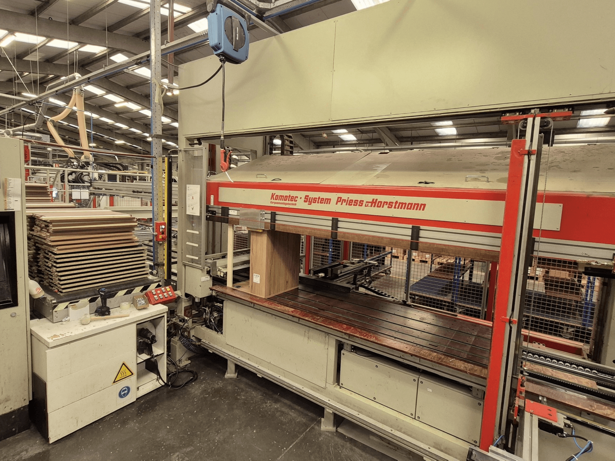 PREISS U HORTSTMANN faneros presas KP-5-CNC, vaizdas iš priekio, matomi sudėti faneros lakštai ir valdymo skydelis.