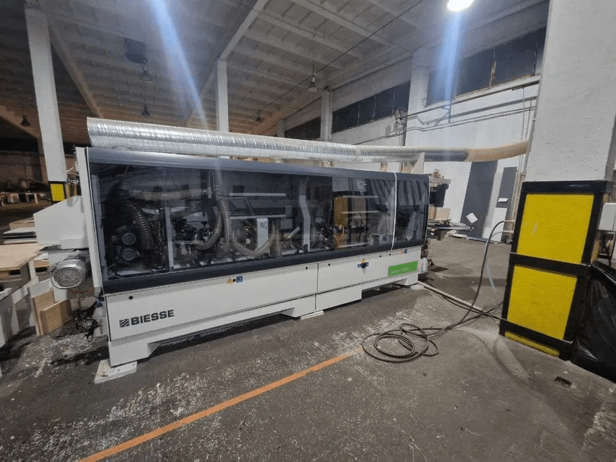 „BIESSE Akron 1440 A“ kraštų apdirbimo staklės dirbtuvėse, su skaidriu gaubtu ir matomais mechaniniais komponentais.
