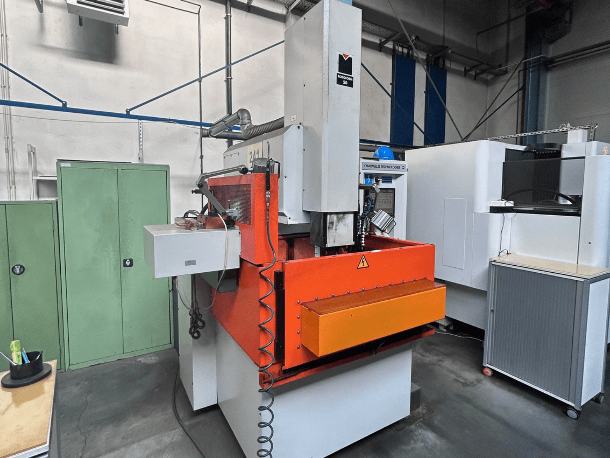 CHARMILLES ROBOFORM 50 Die-Sinking EDM Machine priekinis vaizdas su oranžiniu skydeliu, valdymo sąsaja ir aplinkine įranga.