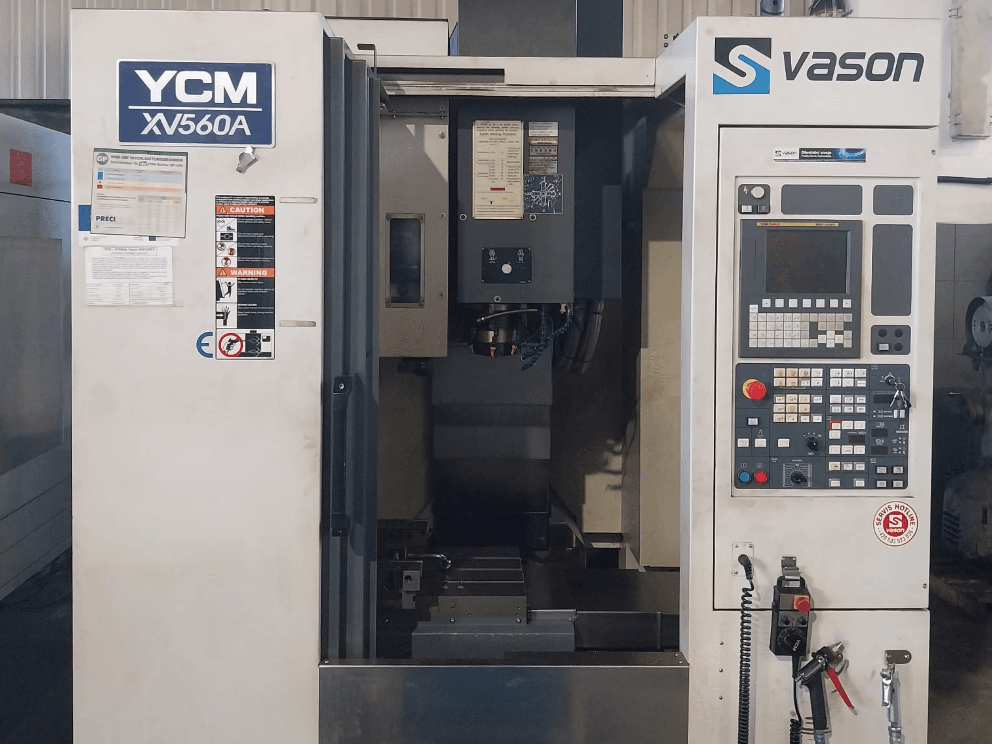 Vertikalaus apdirbimo centro YCM XV 560A priekinis vaizdas, kuriame matomas valdymo skydelis ir darbo stalas su apdirbimo komponentais.