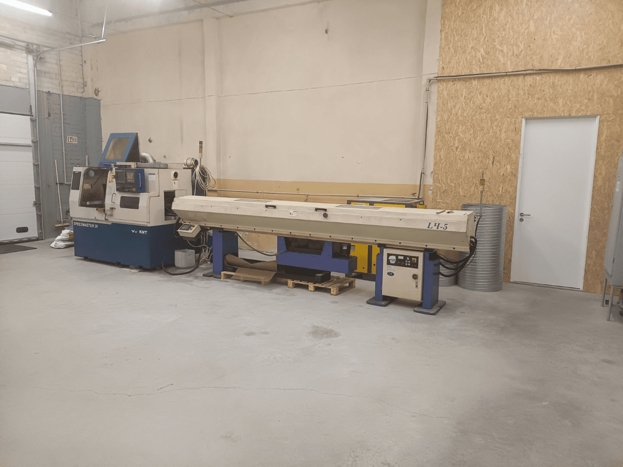 Pramoninės dirbtuvės su KMT Speedmaster 34 mašina ir L4.5, žiūrint iš priekio, su matomais valdikliais ir mechanizmais.
