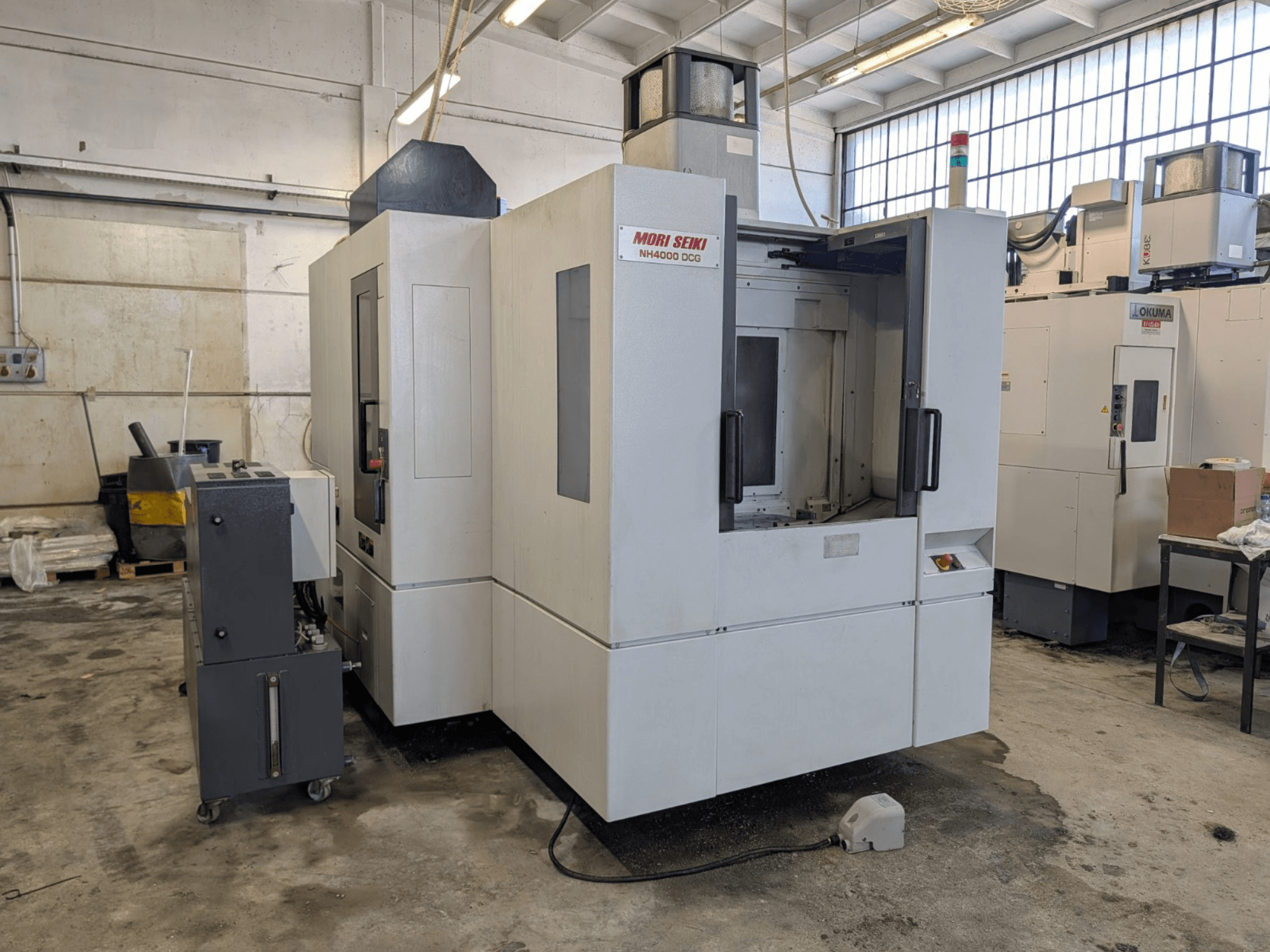 MORI SEIKI NH 4000 DCG horizontalusis apdirbimo centras, vaizdas iš priekio, matomas valdymo skydelis ir darbo zona, pilkos ir baltos spalvos apdaila.