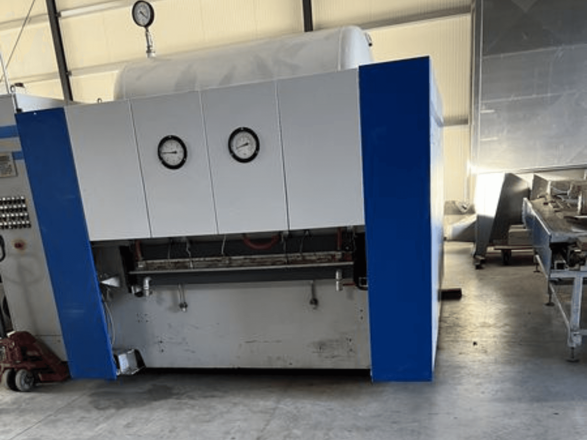 Mėlynos ir baltos spalvos pramoninė mašina su dviem manometrais, vaizdas iš priekio, su valdymo skydeliu ir greta esančia įranga.