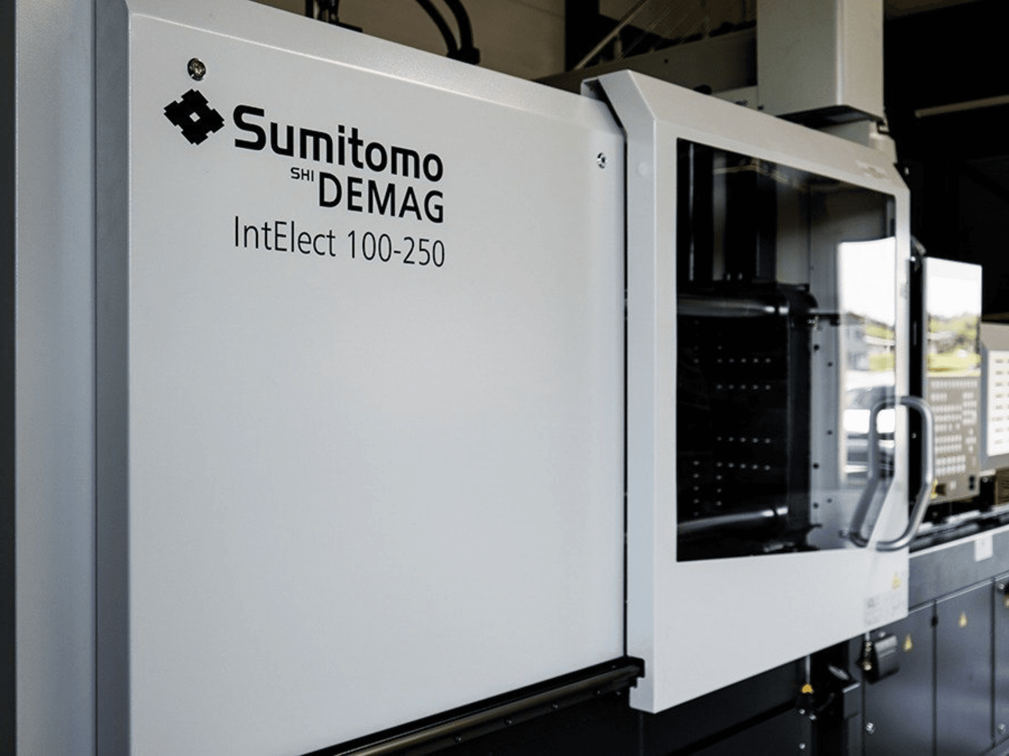 „SUMITOMO SHI DEMAG IntElect 100/250“ elektrinės liejimo mašinos vaizdas iš priekio su valdymo pultu ir saugos įranga.