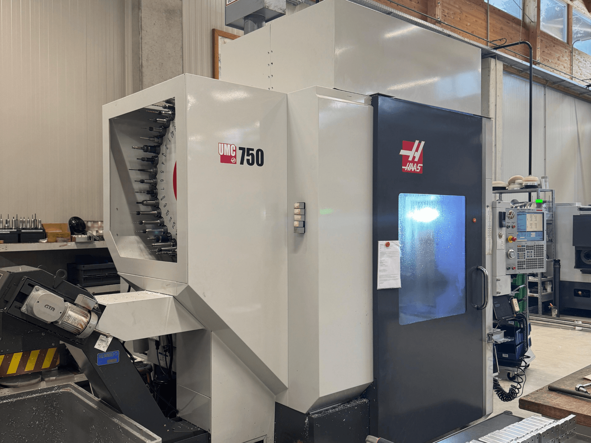 "Haas UMC 750" apdirbimo centras, vaizdas iš priekio, įrankių laikiklis ir valdymo skydelis dirbtuvėse.