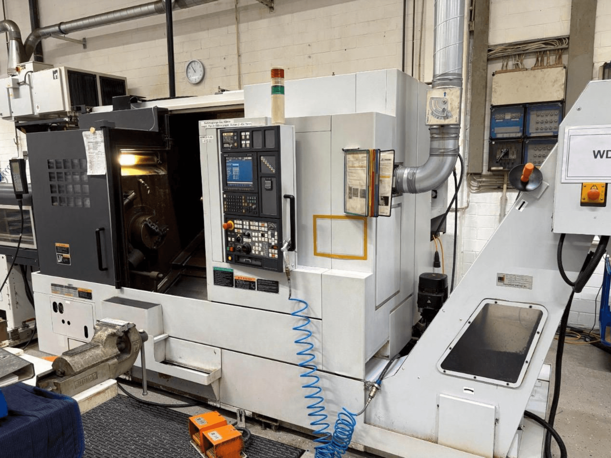 MORI SEIKI NL 2500 SY tekinimo frezavimo centras, priekinis vaizdas, kuriame matomas valdymo skydelis ir apdirbimo zona. Matoma aušinimo skysčio sistema ir priedai.