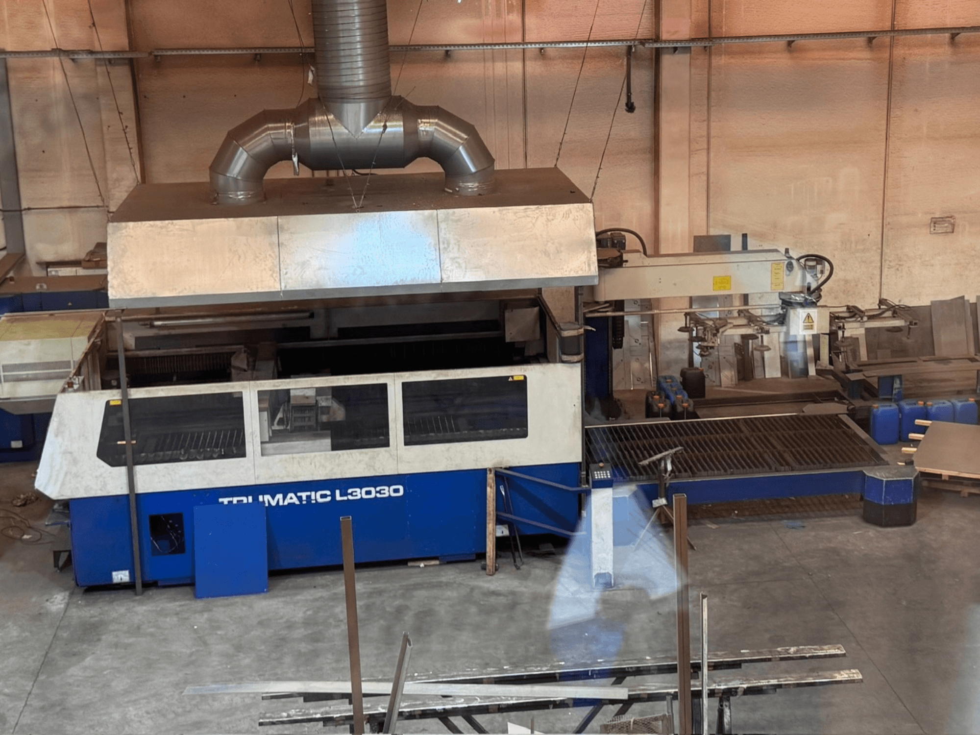 CO₂ lazerio pjovimo staklės „TRUMPF TRUMATIC L3030“ dirbtuvėse, vaizdas iš priekio, kuriame matomas valdymo pultas ir pjovimo stalas.