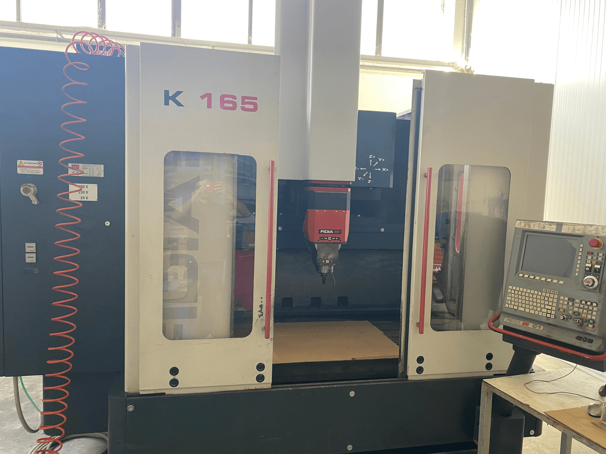 Fidia K 165 CNC staklės su raudonu sukliu ir valdymo skydeliu, žiūrint iš priekio, gerai apšviestose dirbtuvėse.