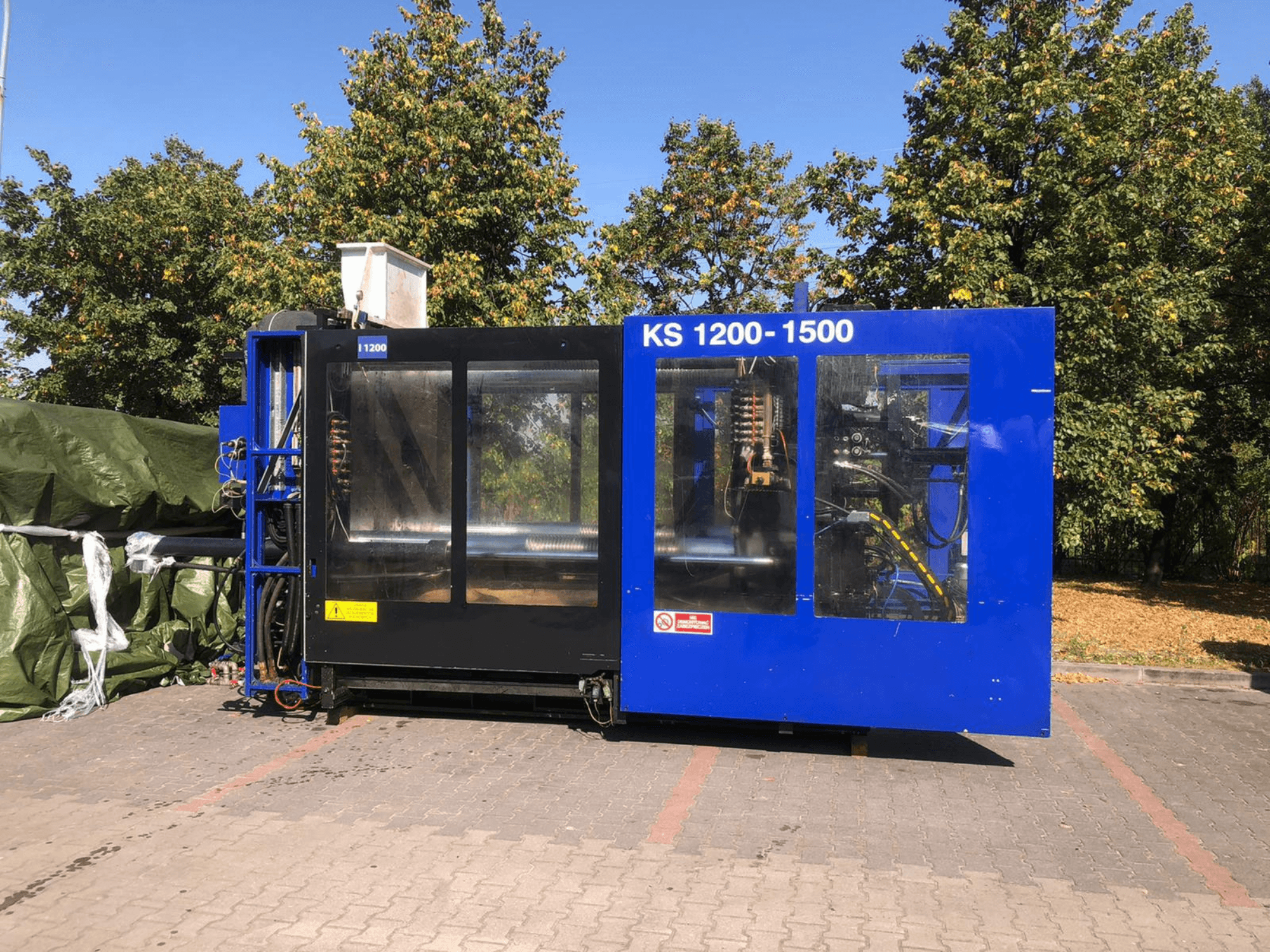 Hidraulinės liejimo mašinos ITALTECH KS 1200 8300 ES, šoninis vaizdas, kuriame matyti valdymo ir mašinų detalės parko aplinkoje.