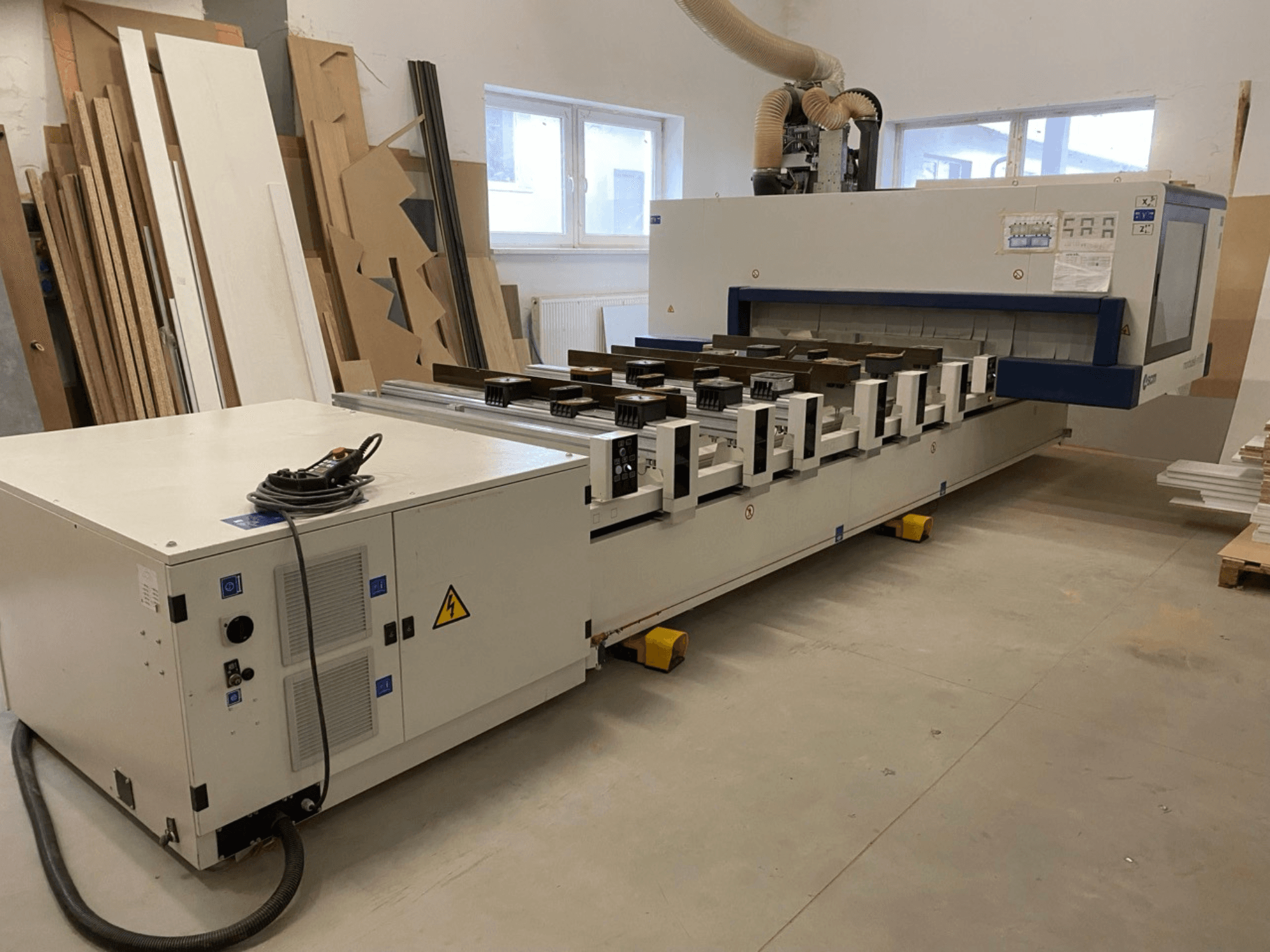 SCM „Morbidelli“ gamintojo M100 CNC medžio apdirbimo centras dirbtuvėse: vaizdas iš priekio su valdymo pultu ir dulkių surinkimo sistema.