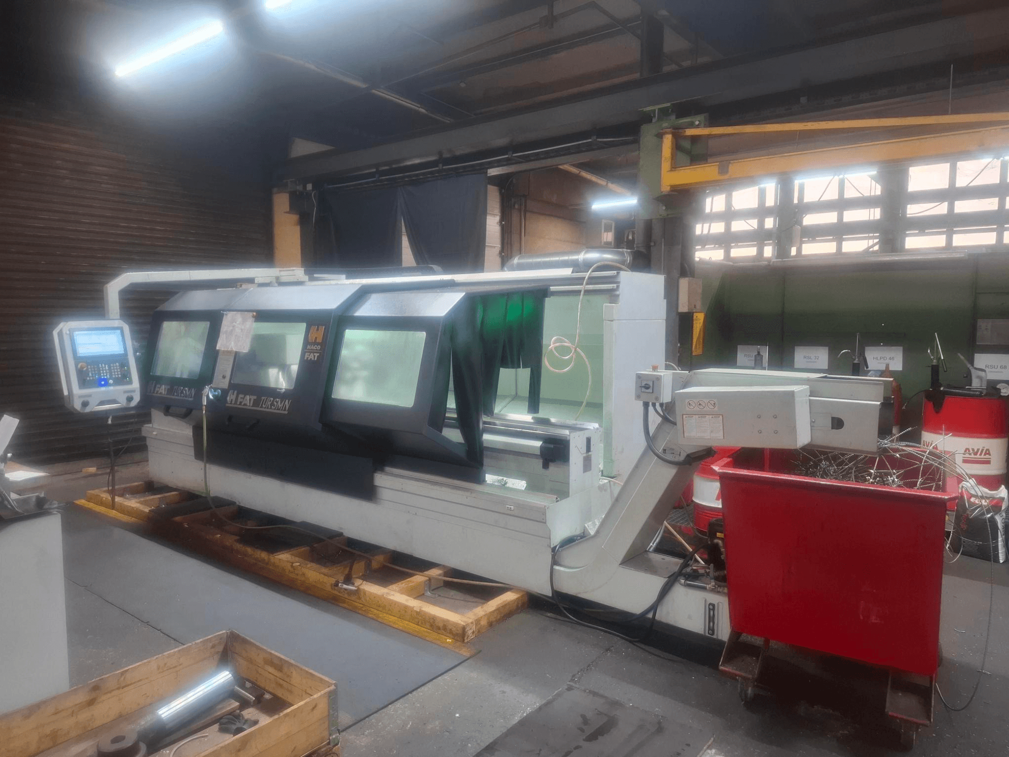 FAT Tursan CNC staklių su valdymo skydeliu, pastatytų ant medinių padėklų dirbtuvėse, vaizdas iš priekio.