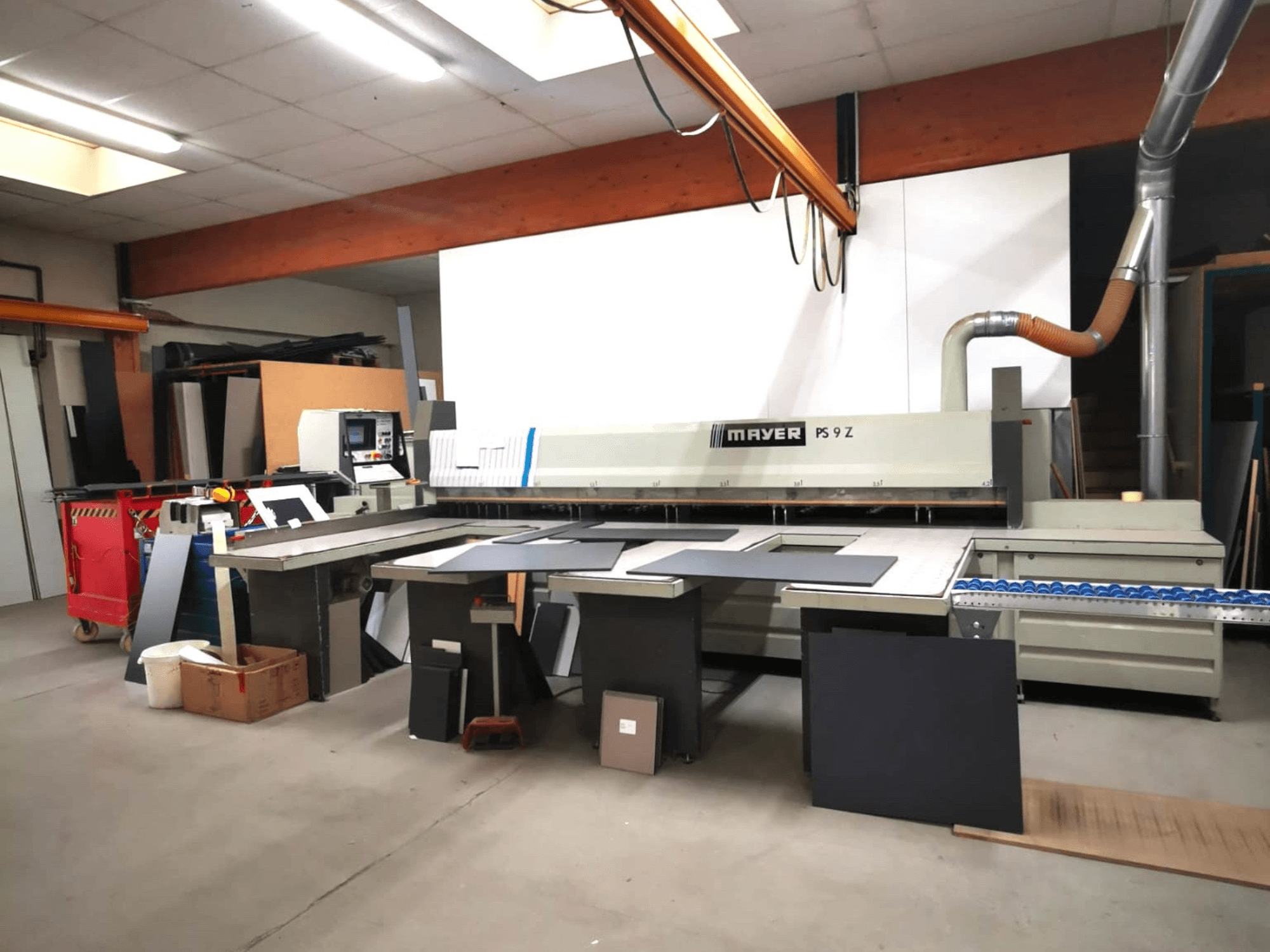 MAYER PS9 Z pjaustymo staklės dirbtuvėse, vaizdas iš priekio, matomos įvairios medžiagos ir konvejerių sistema.