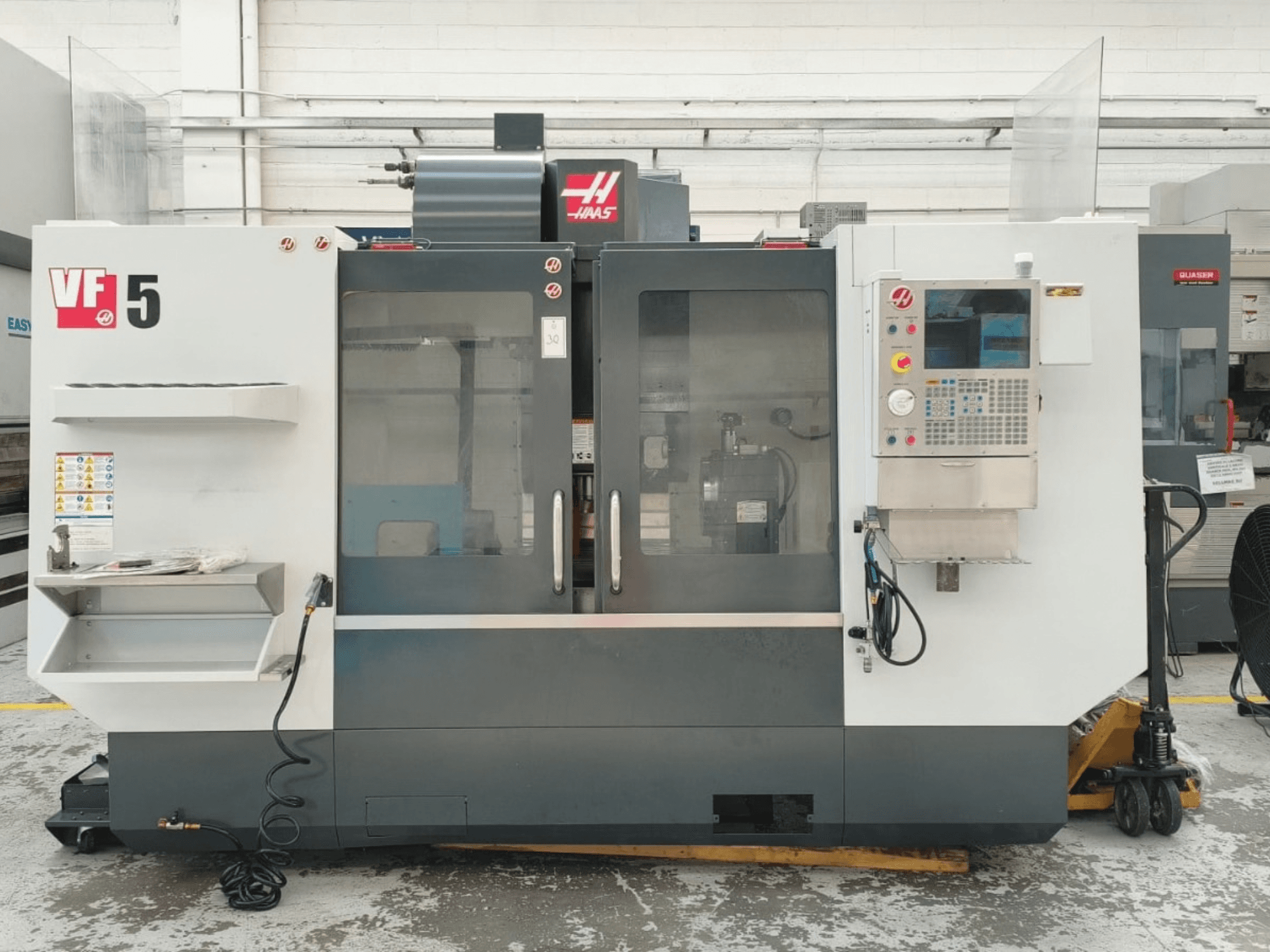 HAAS VF 5/40 vertikalaus apdirbimo centro vaizdas iš priekio, kuriame matomas valdymo pultas ir stiklinės durys.