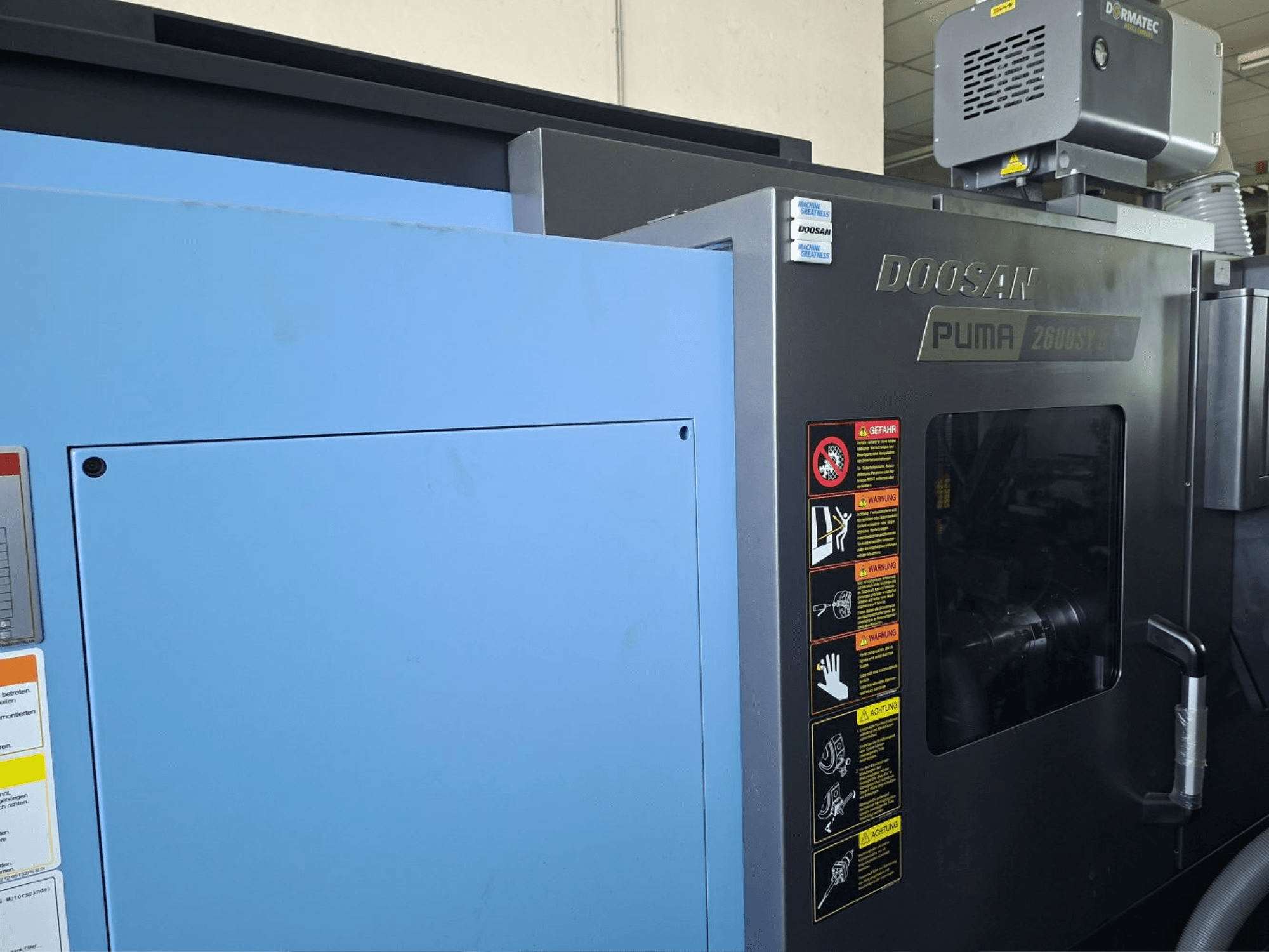 DOOSAN PUMA 2600 SY II horizontalios tekinimo staklės, vaizdas iš priekio, matomos saugos etiketės ir mėlynos plokštės.