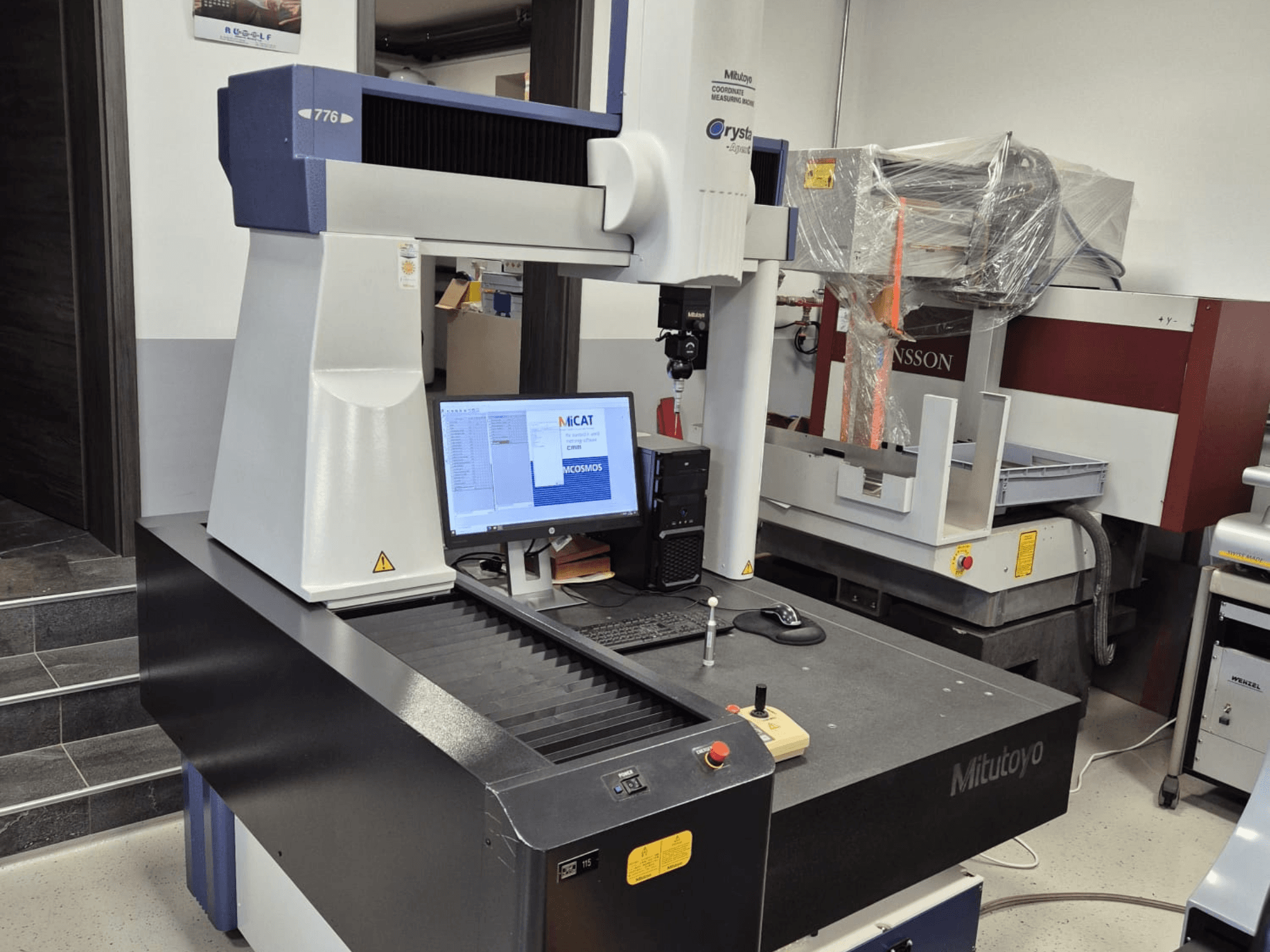 "Mitutoyo" 776 modelio koordinatinės matavimo mašinos vaizdas iš priekio, matomas monitorius su matavimo programine įranga ir valdikliais.