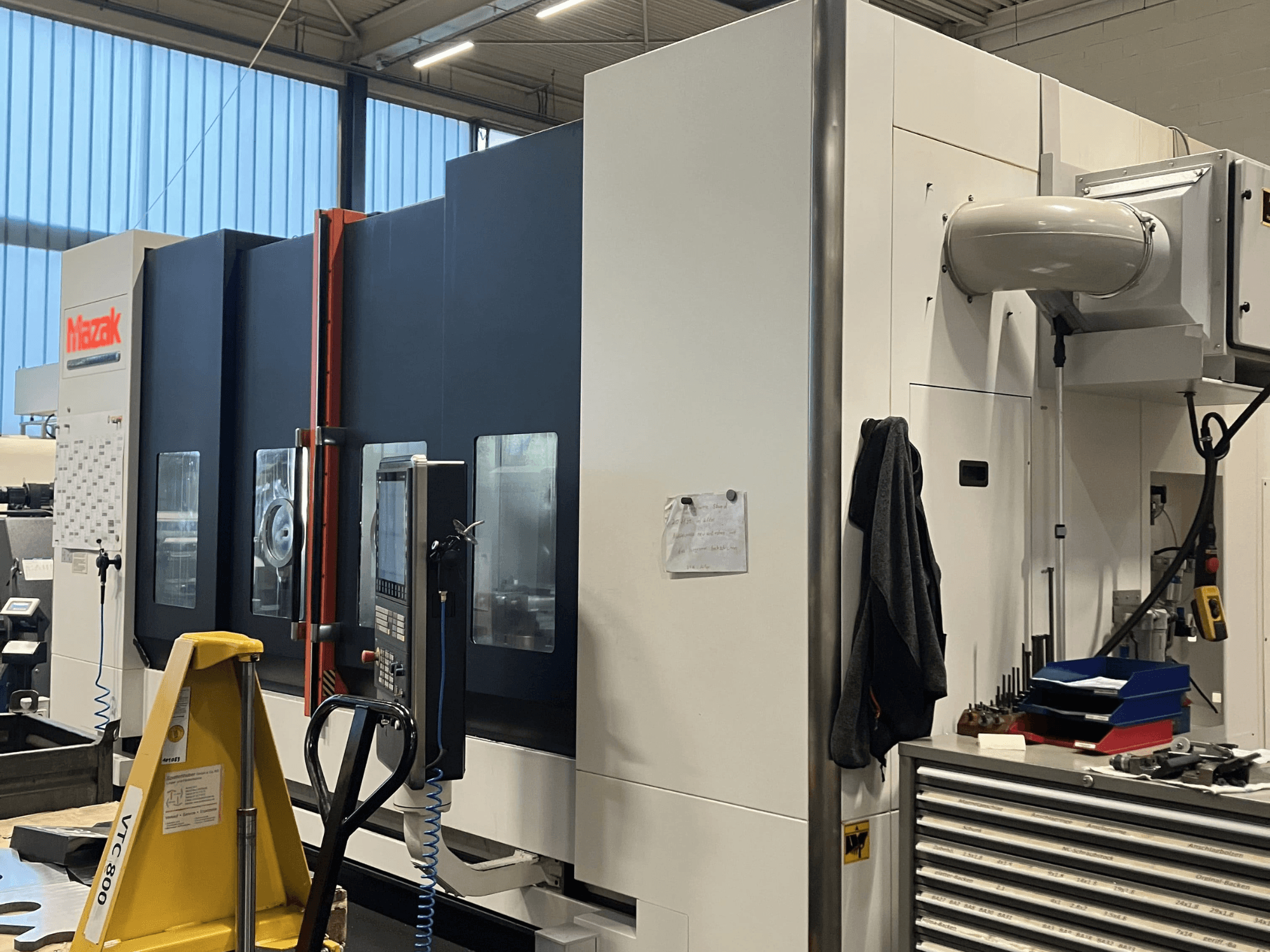 "Mazak" CNC staklės, žiūrint iš šono, demonstruojančios valdymo skydelį ir saugos funkcijas dirbtuvėse.