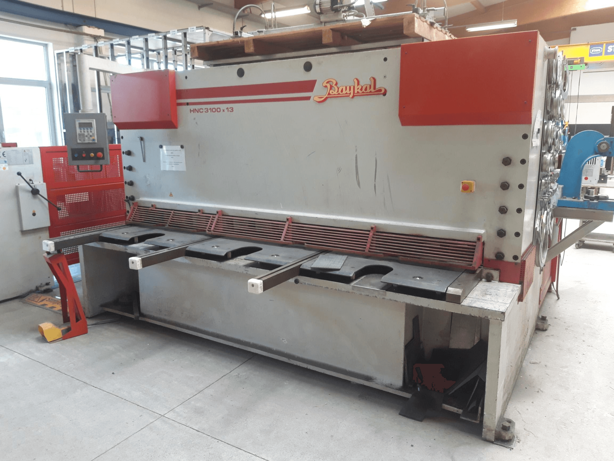 „Baykal HNC 3100x13“ CNC kirpimo staklių vaizdas iš priekio, kuriame matomas valdymo pultas, metalo pjovimo zona ir atliekų surinkimo vieta.