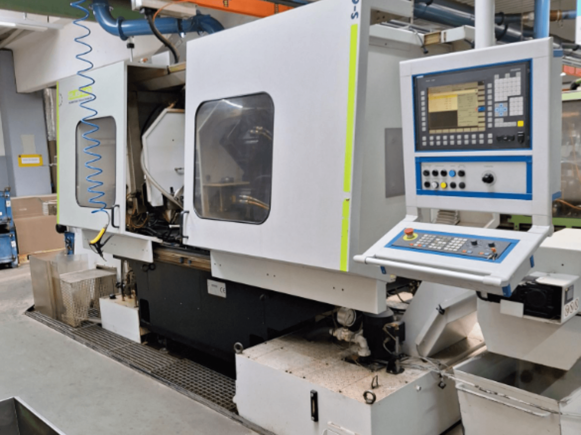 Pramoninės frezavimo staklės su valdymo skydeliu, vaizdas iš šono, su dviem kameromis ir matomomis vamzdynų jungtimis.