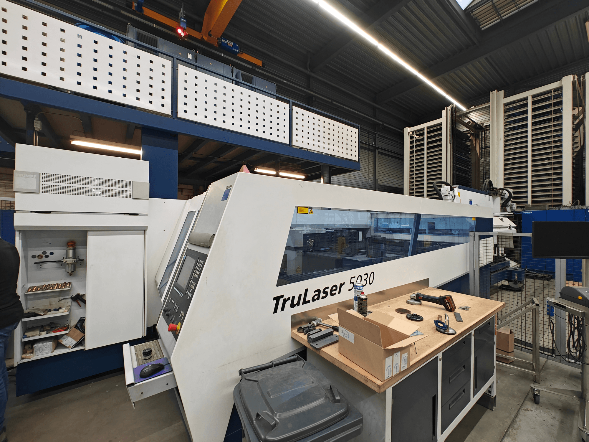 "TruLaser 5030" mašina dirbtuvėse, vaizdas iš priekio, matomas valdymo skydelis, apsuptas įrankių ir įrangos.