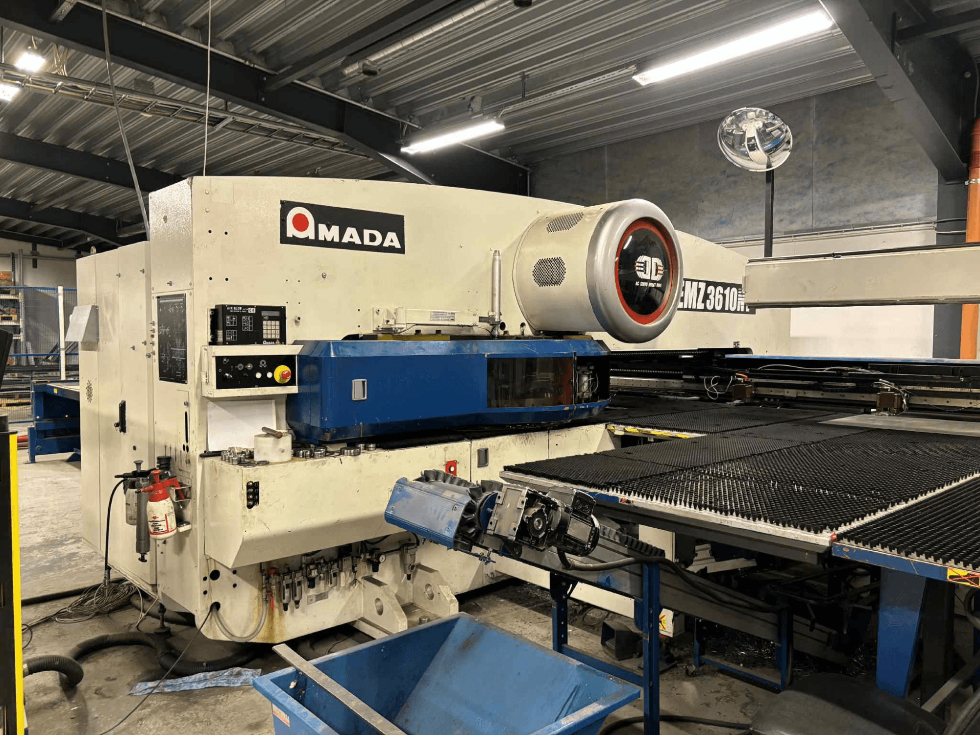 "Amada EMZ3610H" perforatorius, žiūrint iš priekio; yra valdymo elementai, mėlyna lova ir saugos įranga.