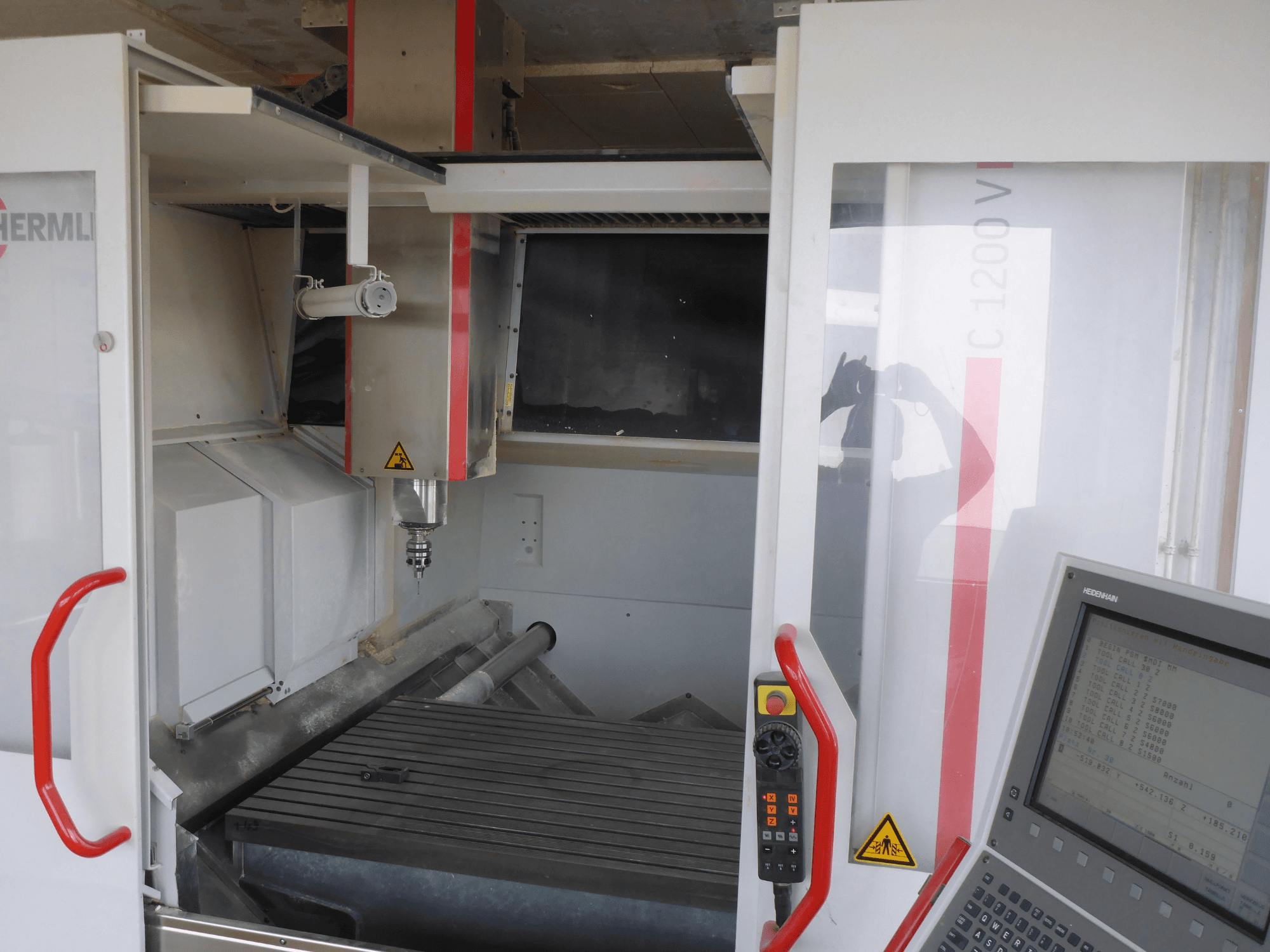 HERMLE C 1200 vertikalaus apdirbimo centro interjeras, kuriame matomas įrankių laikiklis, valdymo skydelis ir darbo stalas iš priekio.