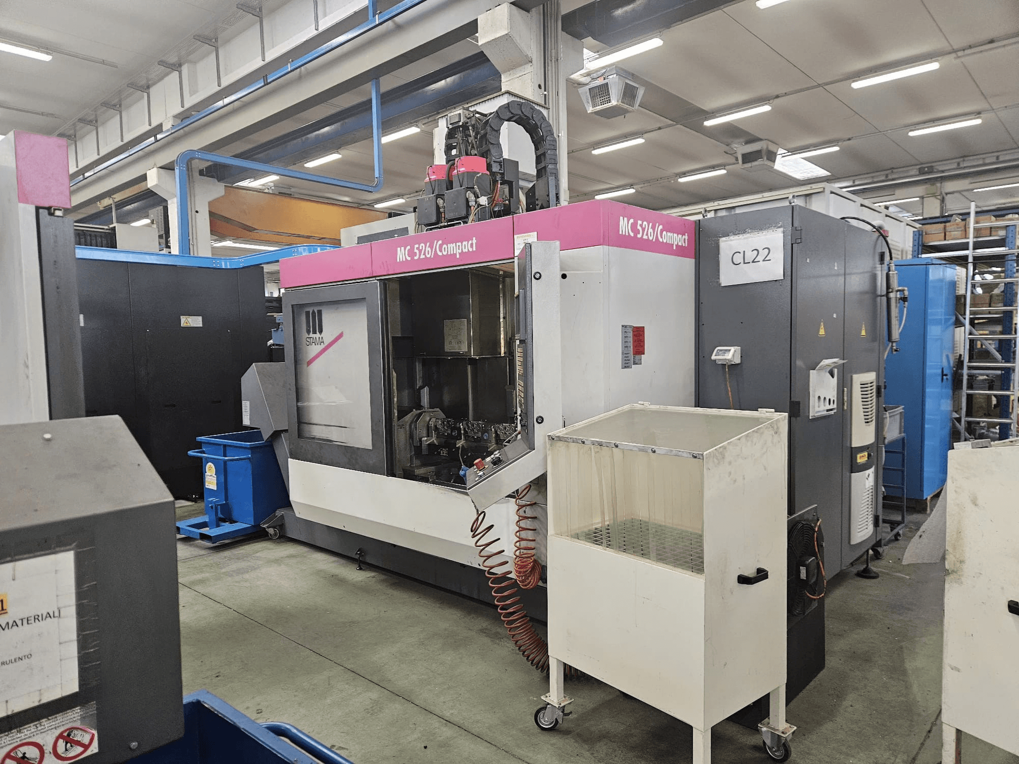 Kompaktinės CNC staklės MC 526 iš "Stama", šoninis vaizdas, kuriame matyti valdymo skydelis, aušinimo skysčio bakas ir gretimos mašinos.