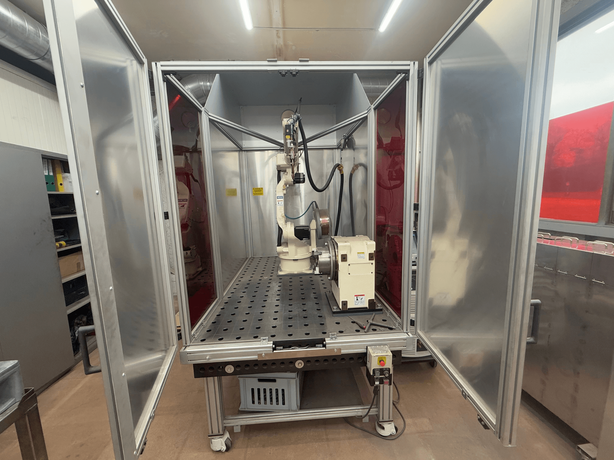 Suvirinimo robotas OTC Daihen EASY ARC V02.04 metaliniame korpuse, žiūrint iš priekio, su šarnyrine ranka ir valdymo skydeliu.