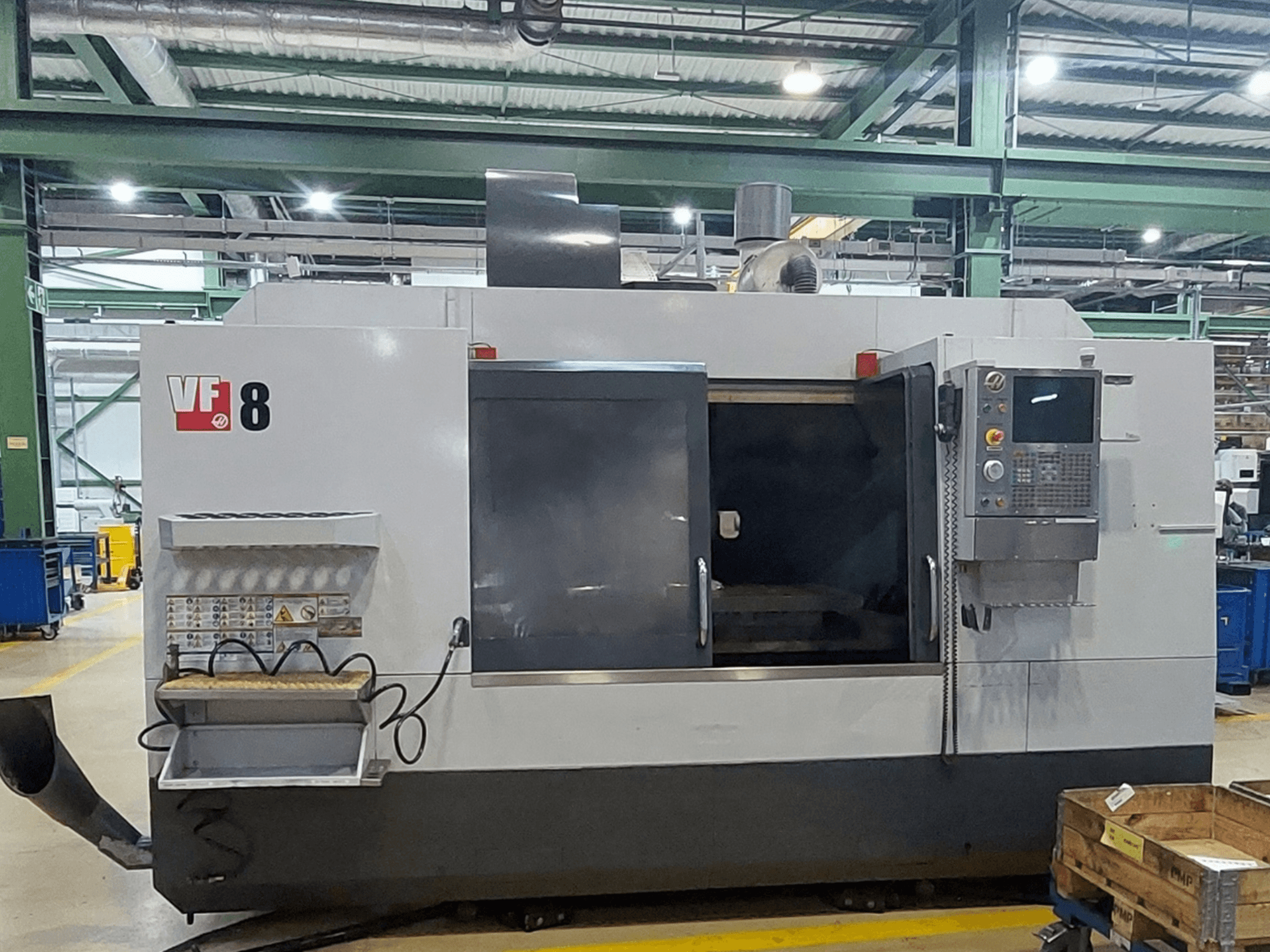 Vertikalusis apdirbimo centras „HAAS VF-8“, vaizdas iš priekio; jame matomas valdymo pultas ir pakrovimo zona, skirta tiksliems apdirbimo darbams atlikti.