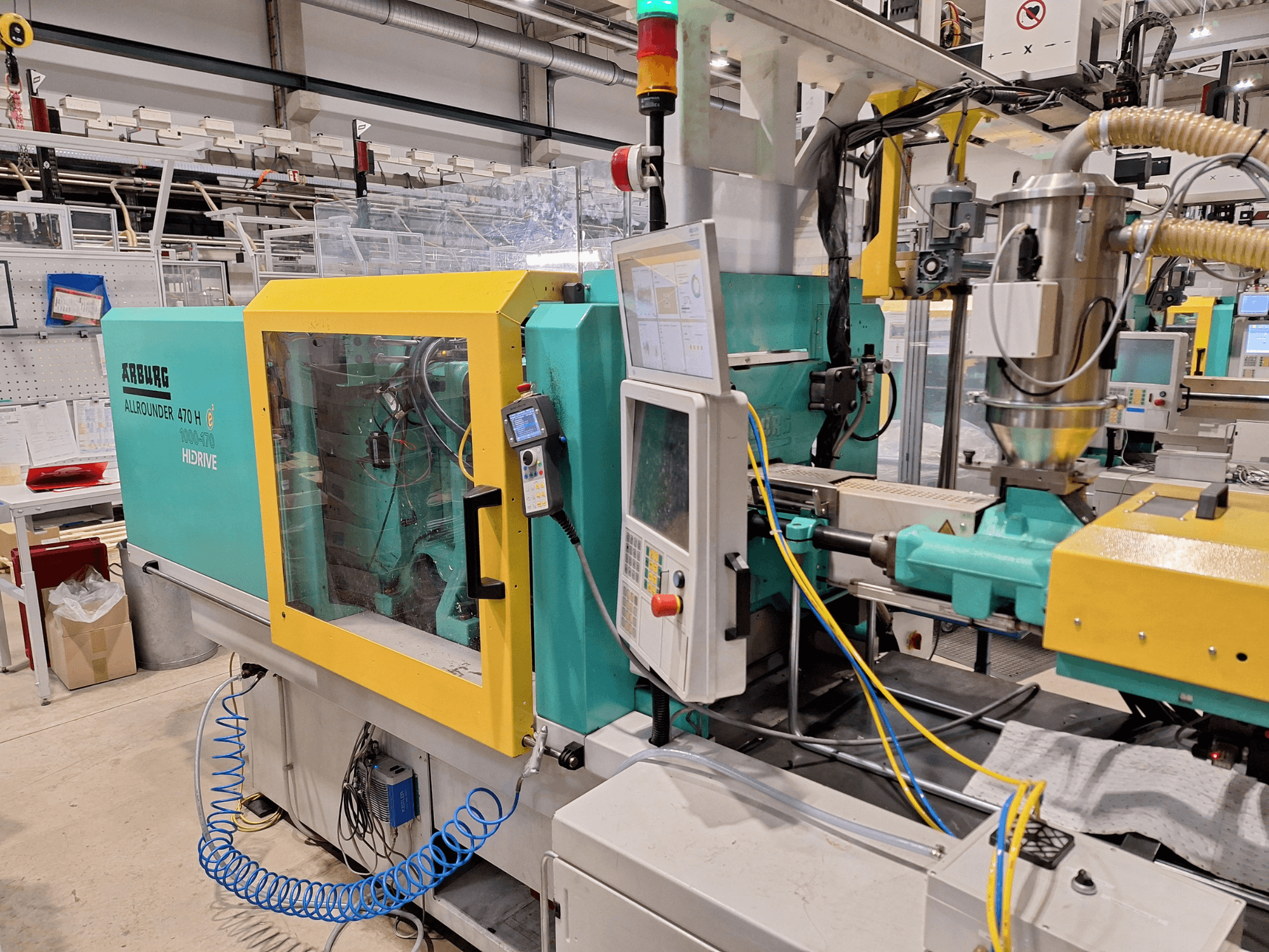 Arburg 470 H 1000-170 hidraulinė liejimo mašina, šoninis vaizdas, kuriame matomas valdymo skydelis ir padavimo sistema.