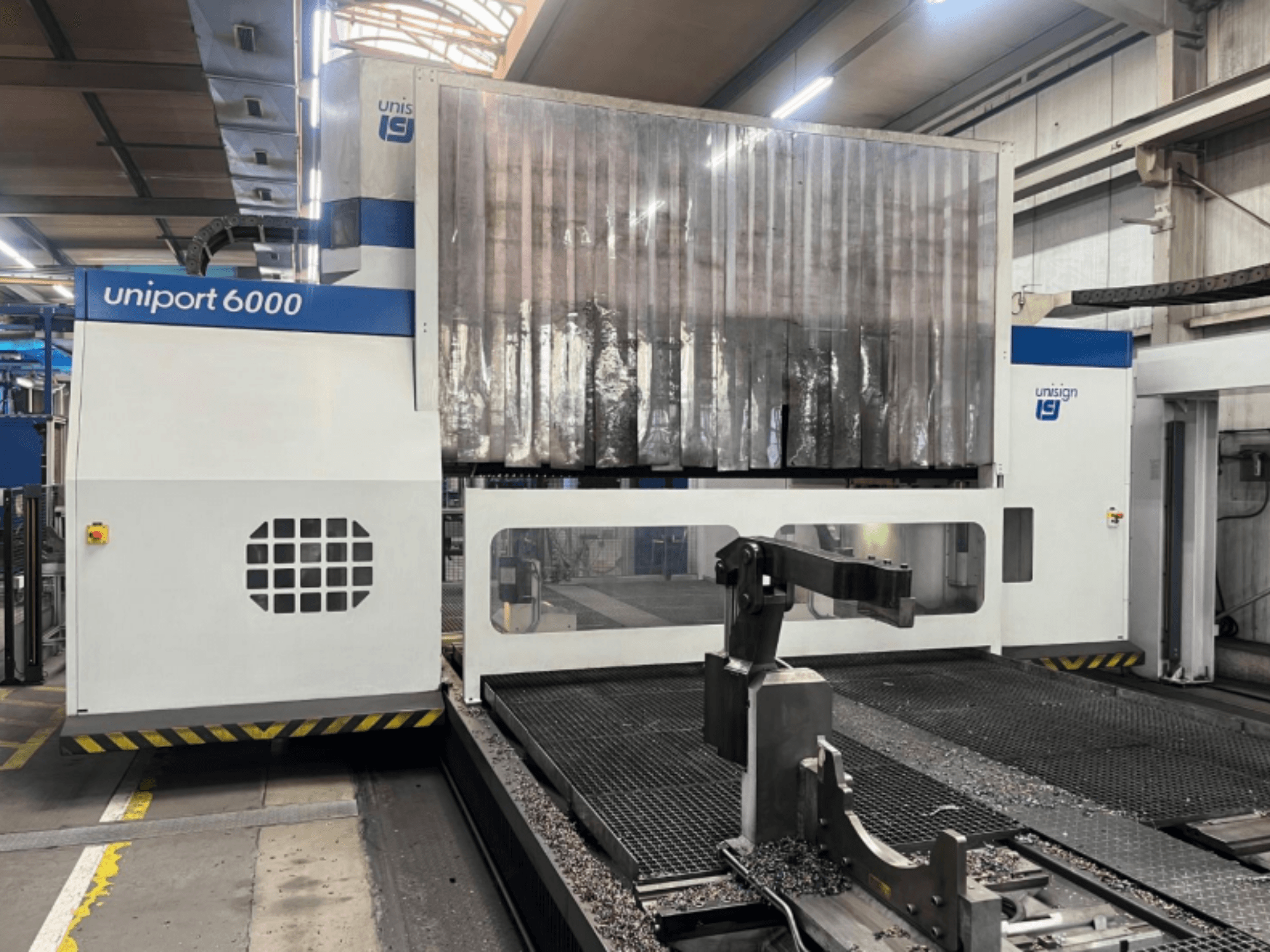 Portalinės frezavimo staklės "Unisign uniport 6000", vaizdas iš priekio, matoma staklių konstrukcija ir pjovimo zona su metalo drožlėmis.