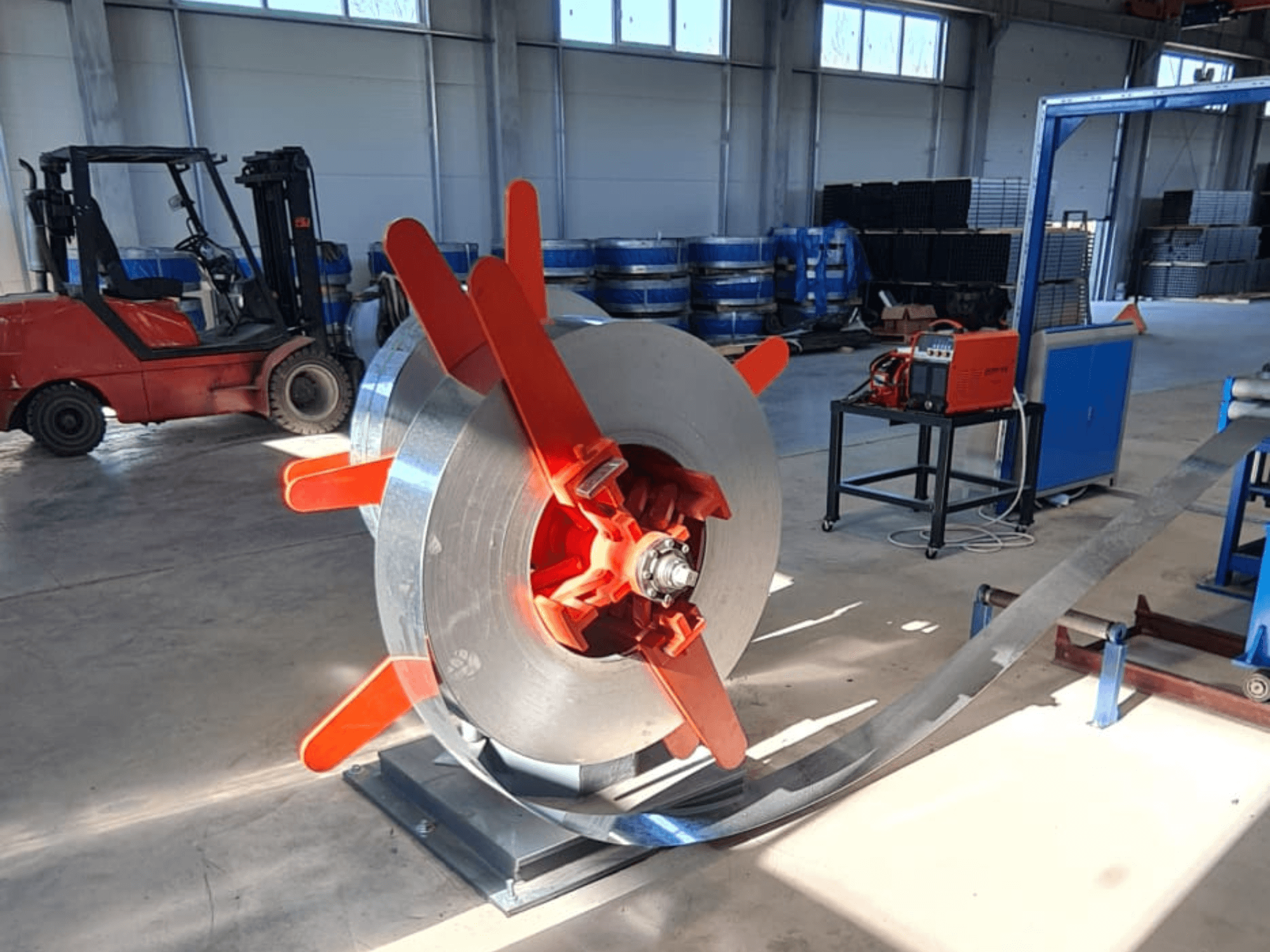 Metalinė ritė su raudonomis rankenėlėmis ant stovo, žiūrint kampu. Pramoninis fonas su mašinomis ir krautuvu.