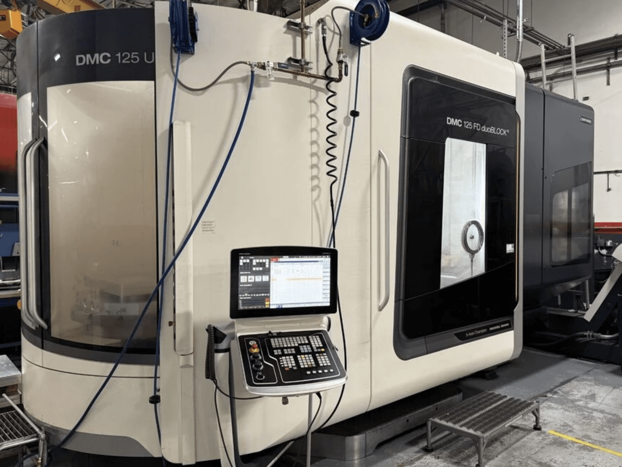Universalus apdirbimo centras „DMG MORI DMC 125 U duoBLOCK“, vaizdas iš priekio su valdymo pultu ir atspindinčiais paviršiais.