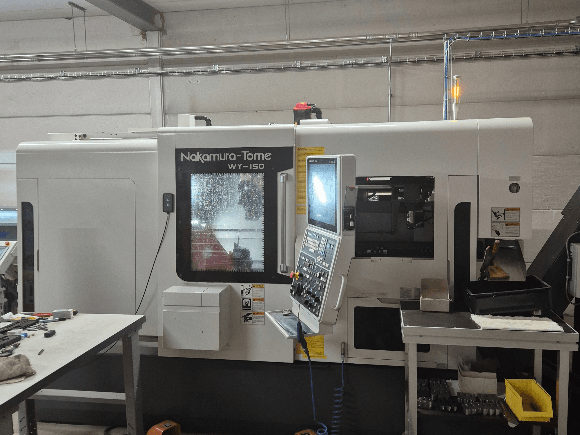 Nakamura-Tome WY-150 CNC tekinimo staklės iš šono, su valdymo skydeliu, permatomu langu ir matoma darbo zona.