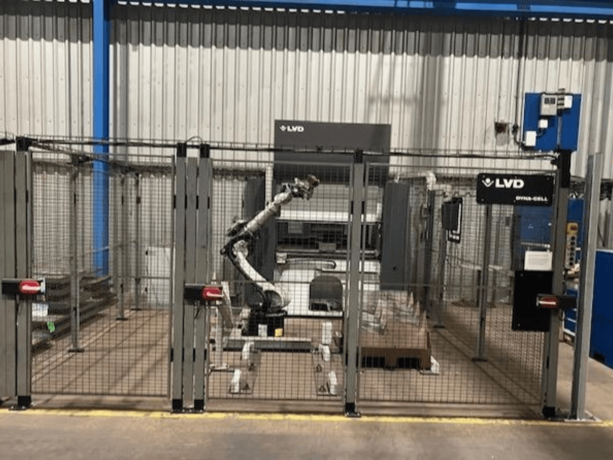 LVD "Dyna-Cell" robotinė darbo vieta aptvertoje patalpoje, vaizdas iš priekio, su robotine ranka ir valdymo pultu.