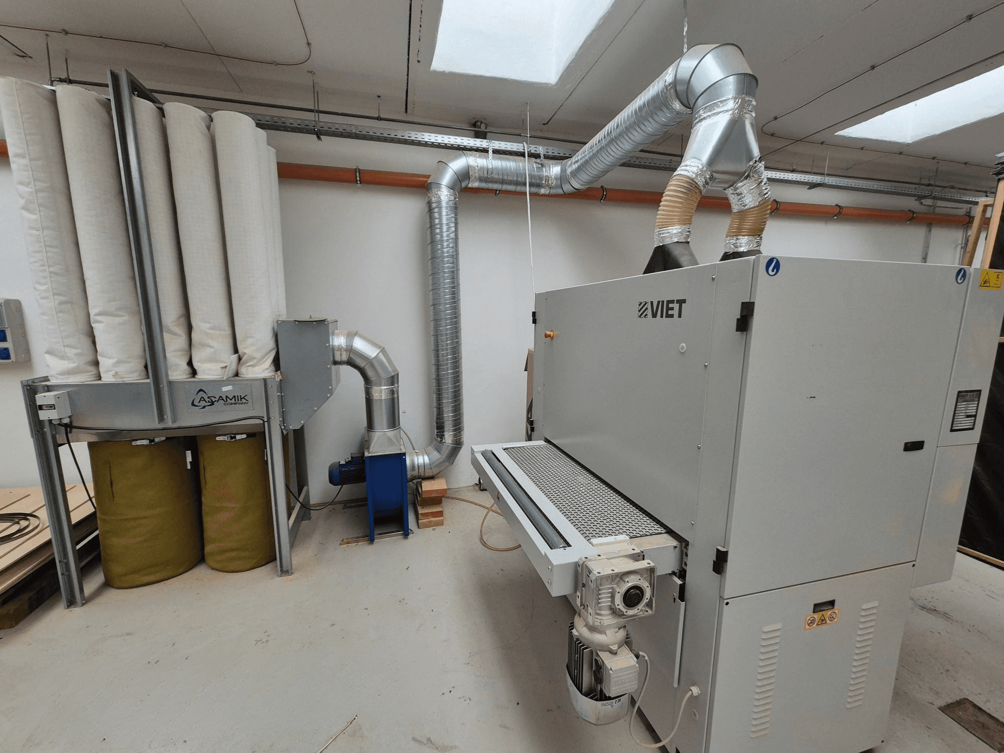 "Viet" dulkių ištraukimo sistema su cilindriniais filtrais ir sidabriniu išmetimo vamzdžiu, žiūrint iš priekio dirbtuvėse.