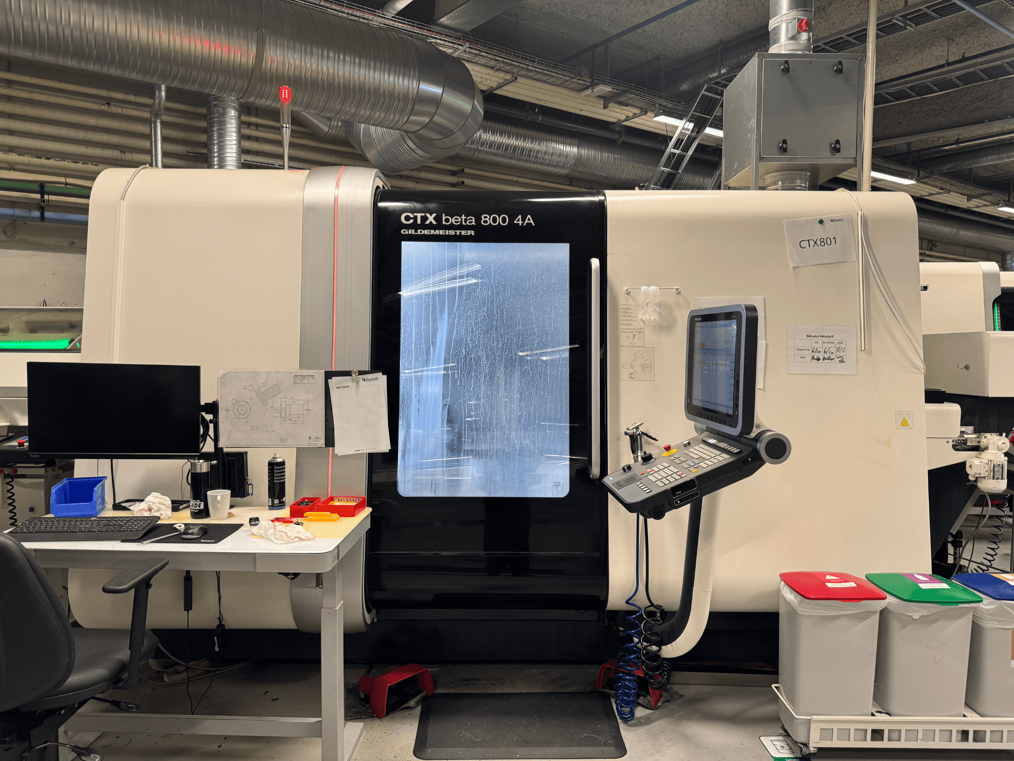 CTX beta 800 4A staklės su valdymo pultu ir monitoriumi, vaizdas iš šono, dirbtuvėse su biuro įranga ir spalvotomis šiukšliadėžėmis.