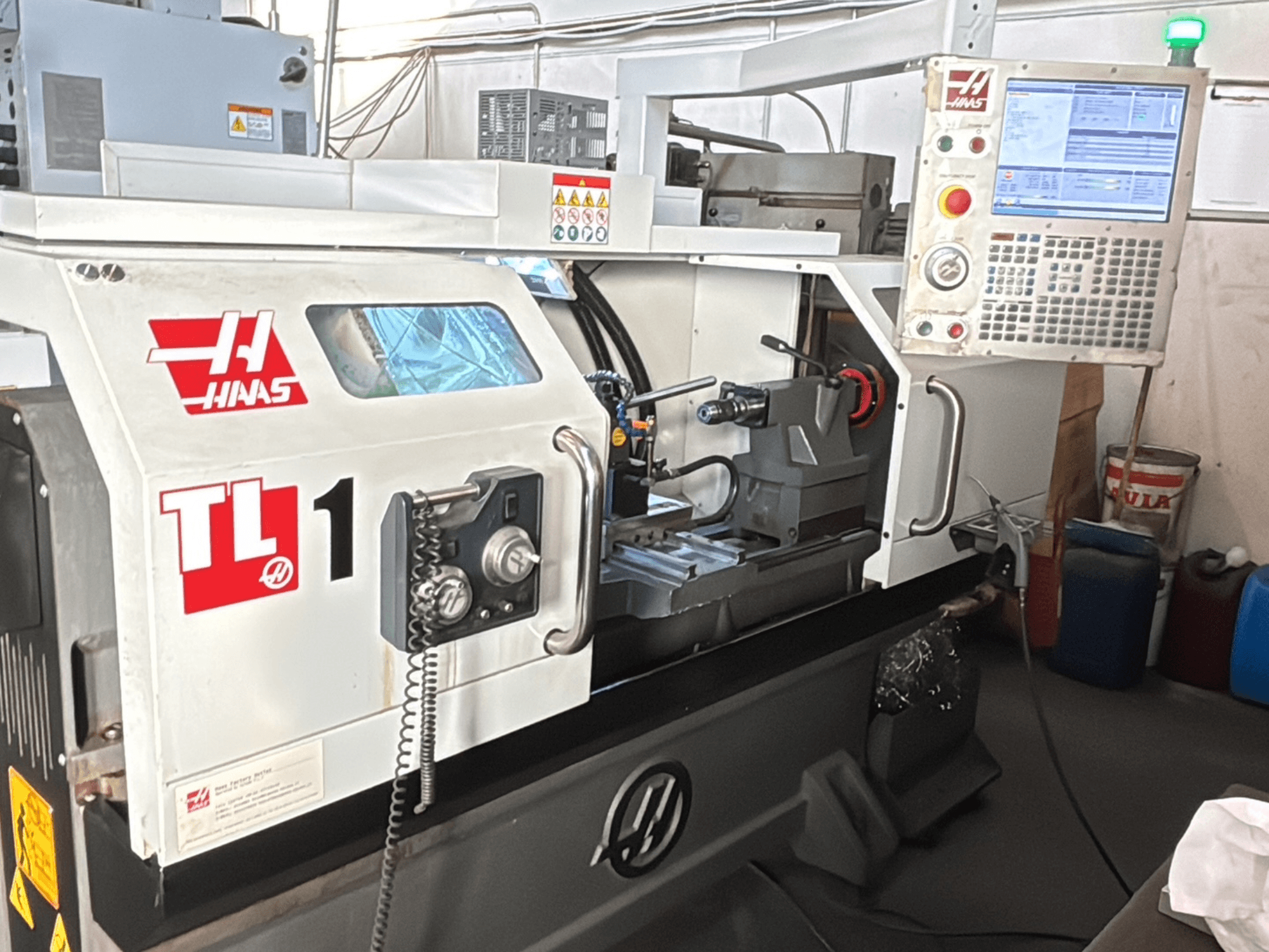 Haas TL-1 CNC tekinimo staklės, vaizdas iš priekio, valdymo skydelis su ekranu, įrankių laikiklis ir saugos etiketės.