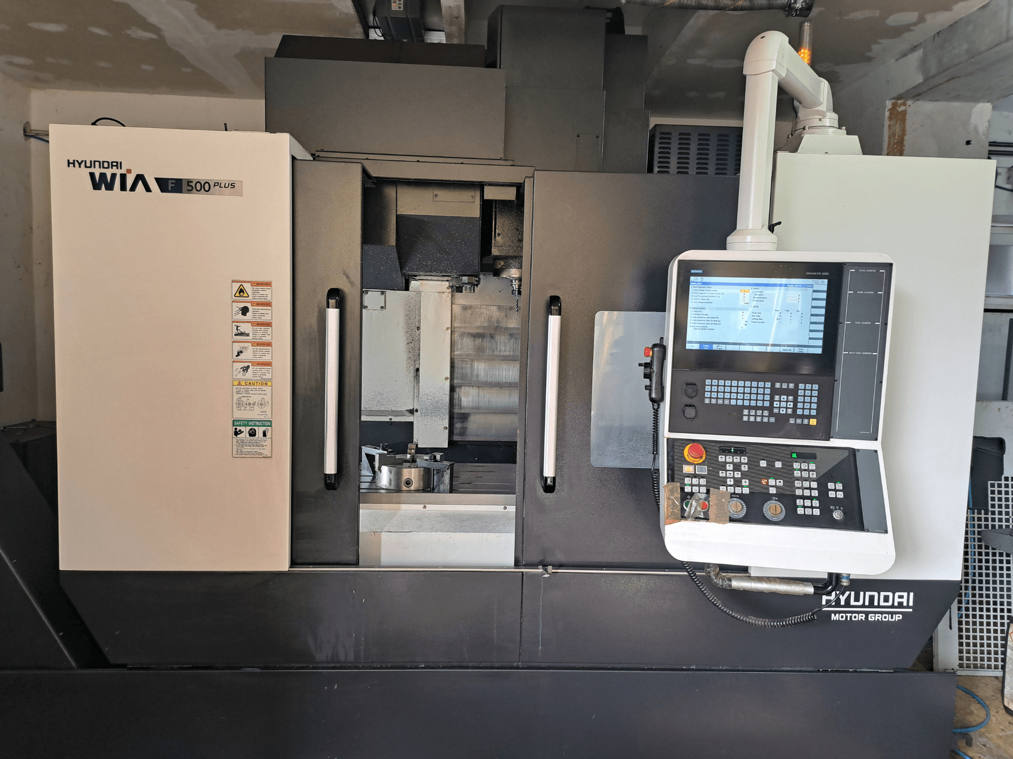 "Hyundai WIA F500 Plus CNC" staklės iš priekio, su skaitmeniniu valdymo skydeliu ir saugos etiketėmis.