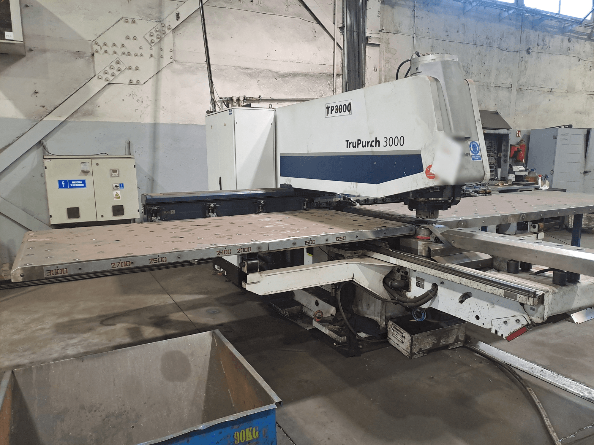 "TruPunch 3000 CNC" staklės su didele metaline plokštele ir matavimo žymomis pramoninėje aplinkoje, parodytos iš priekio.